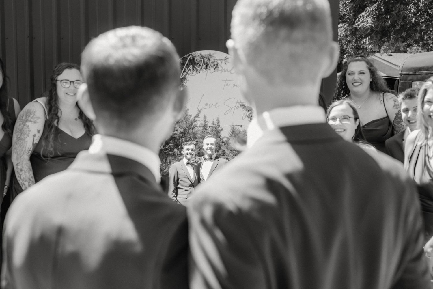Black and white photo of two grooms facing wedding guests during an outdoor ceremony.