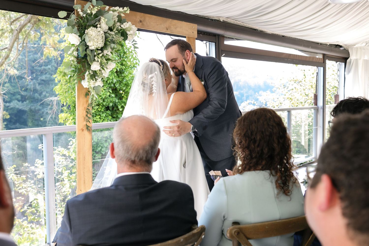 Wedding ceremony under a white tent canopy with forest views in the background.