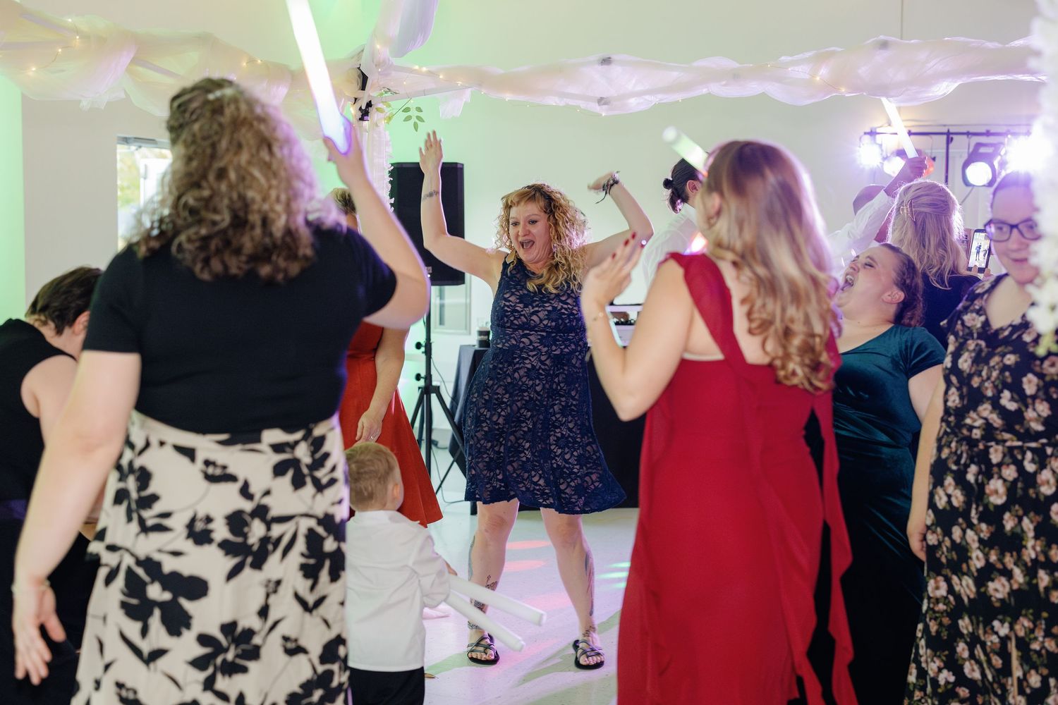 Wedding reception dance floor filled with guests enjoying themselves under colorful lighting.