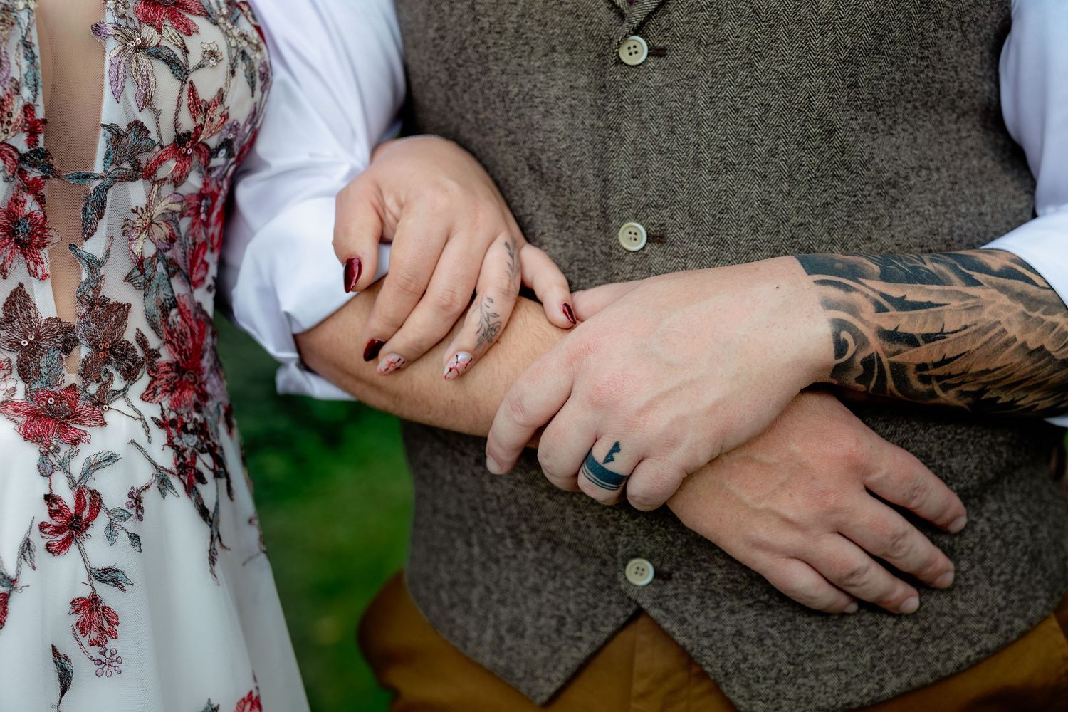 Close-up details of wedding rings and hands showing intricate tattoo artwork.