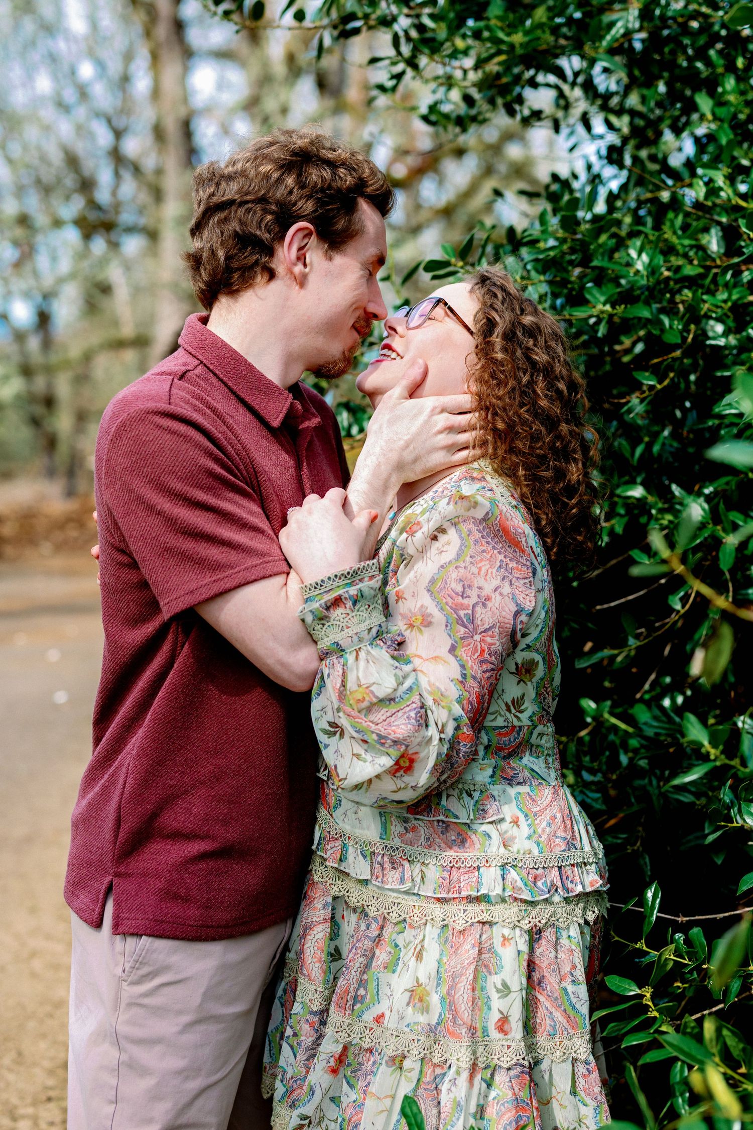 A romantic couple sharing tender moments in a garden setting wearing burgundy and floral print clothing.