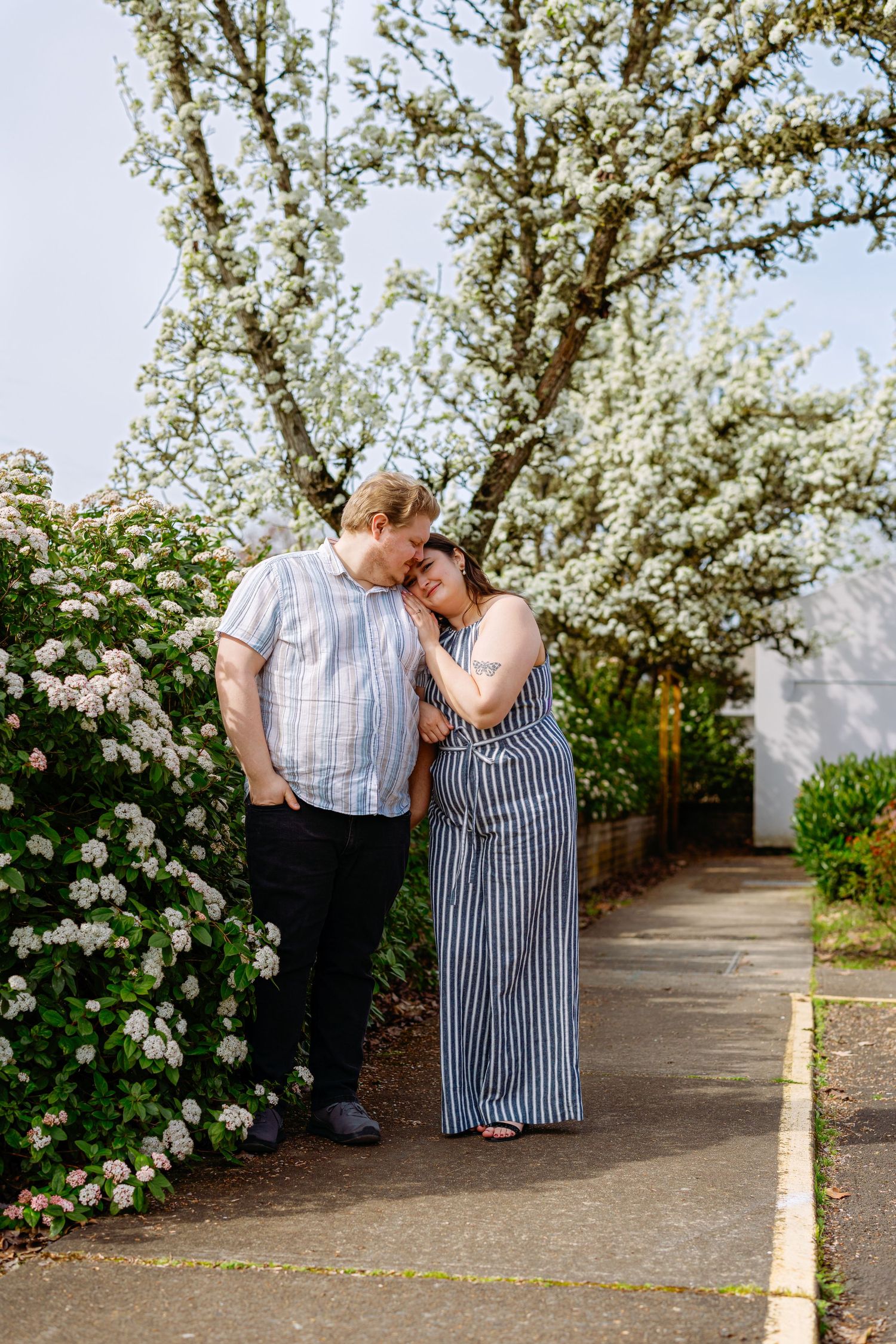 A romantic moment captured under blooming white cherry blossom trees along a garden pathway.