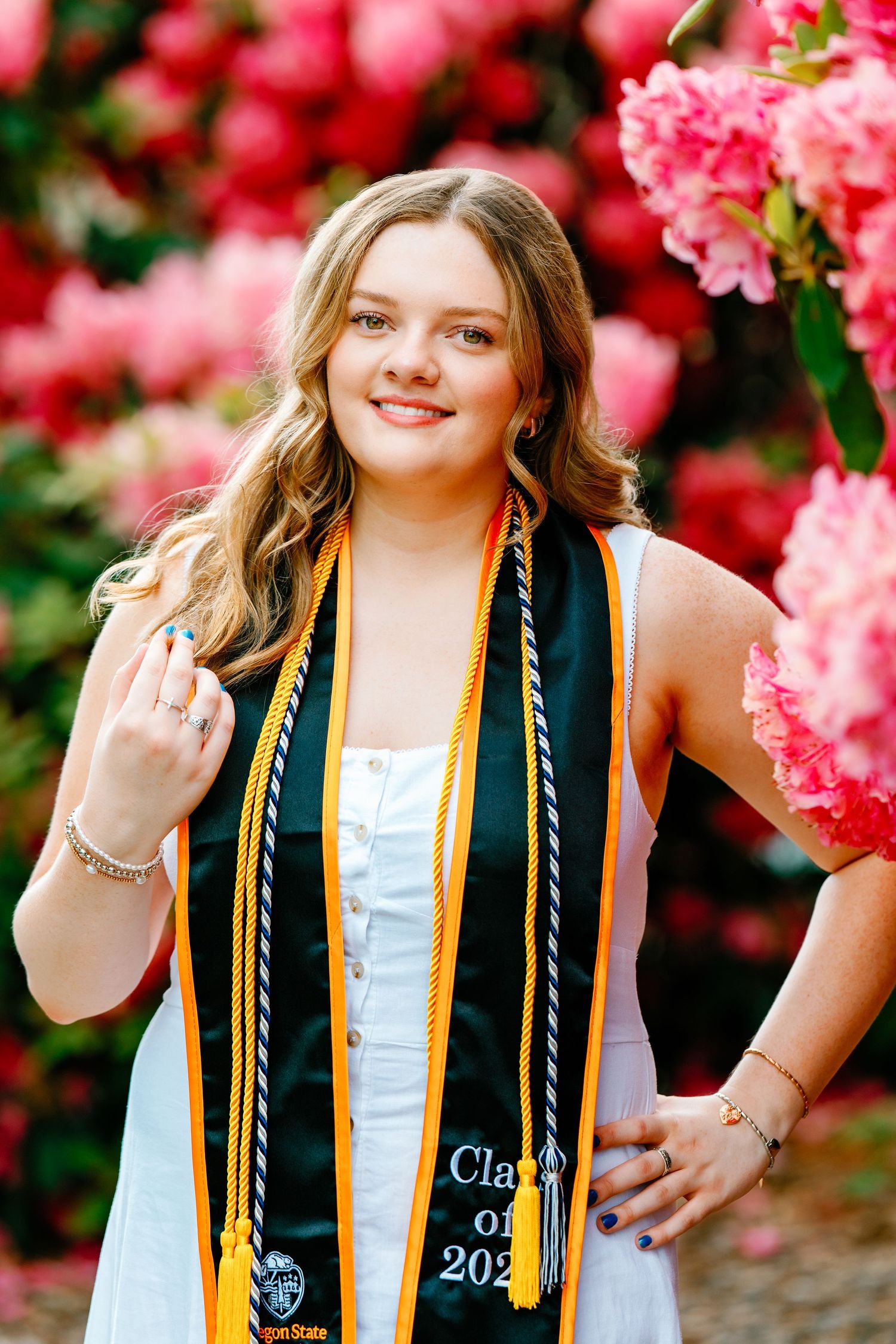 Smiling female graduate wearing green and gold graduation stole with pink flowers in background.