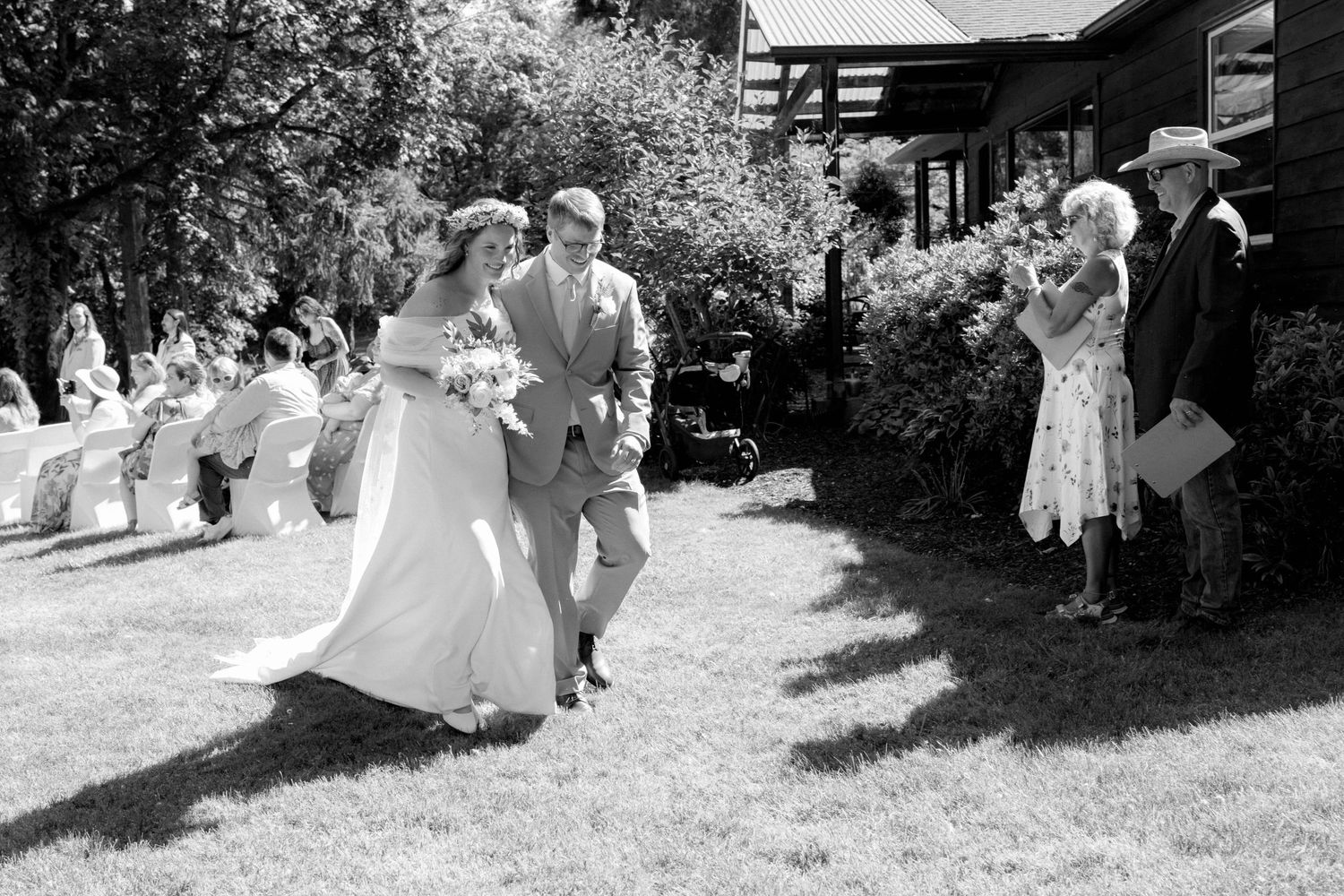 Black and white photo of a bride and groom walking down the aisle at an outdoor wedding ceremony.