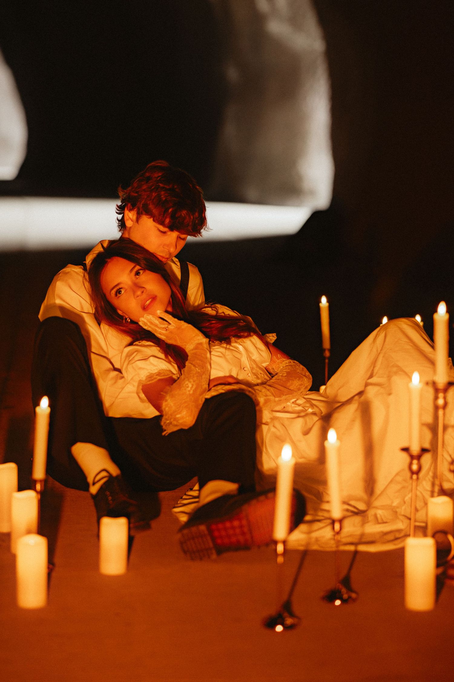 A person in orange attire lights candles arranged in a row creating a warm atmospheric glow.