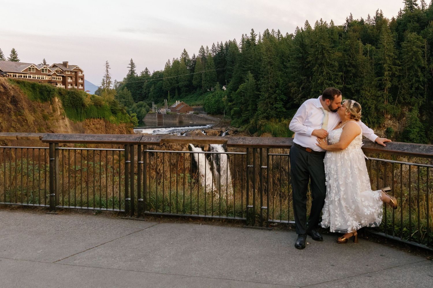 A couple embraces during their wedding photoshoot at Snoqualmie Falls with evergreen forest and waterfall views.