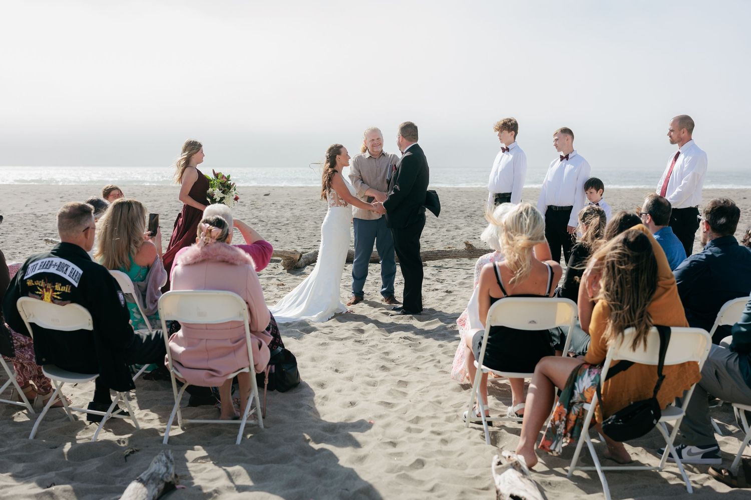 An intimate beach wedding ceremony with guests seated on chairs in the sand.