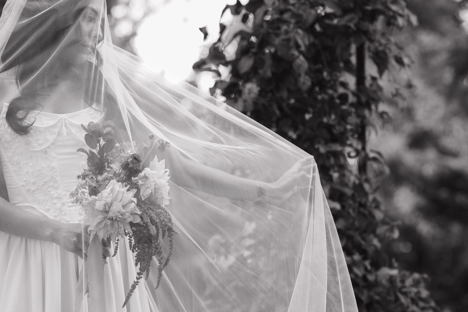 Black and white detail of a bride's veil and bouquet creating an ethereal effect.