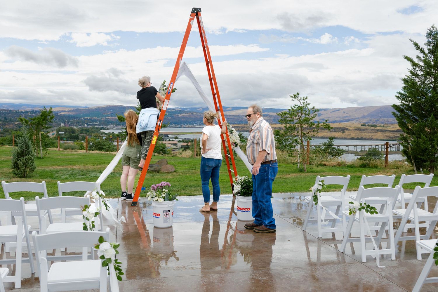 Wedding ceremony setup with white chairs and orange arch overlooking a scenic mountain landscape.