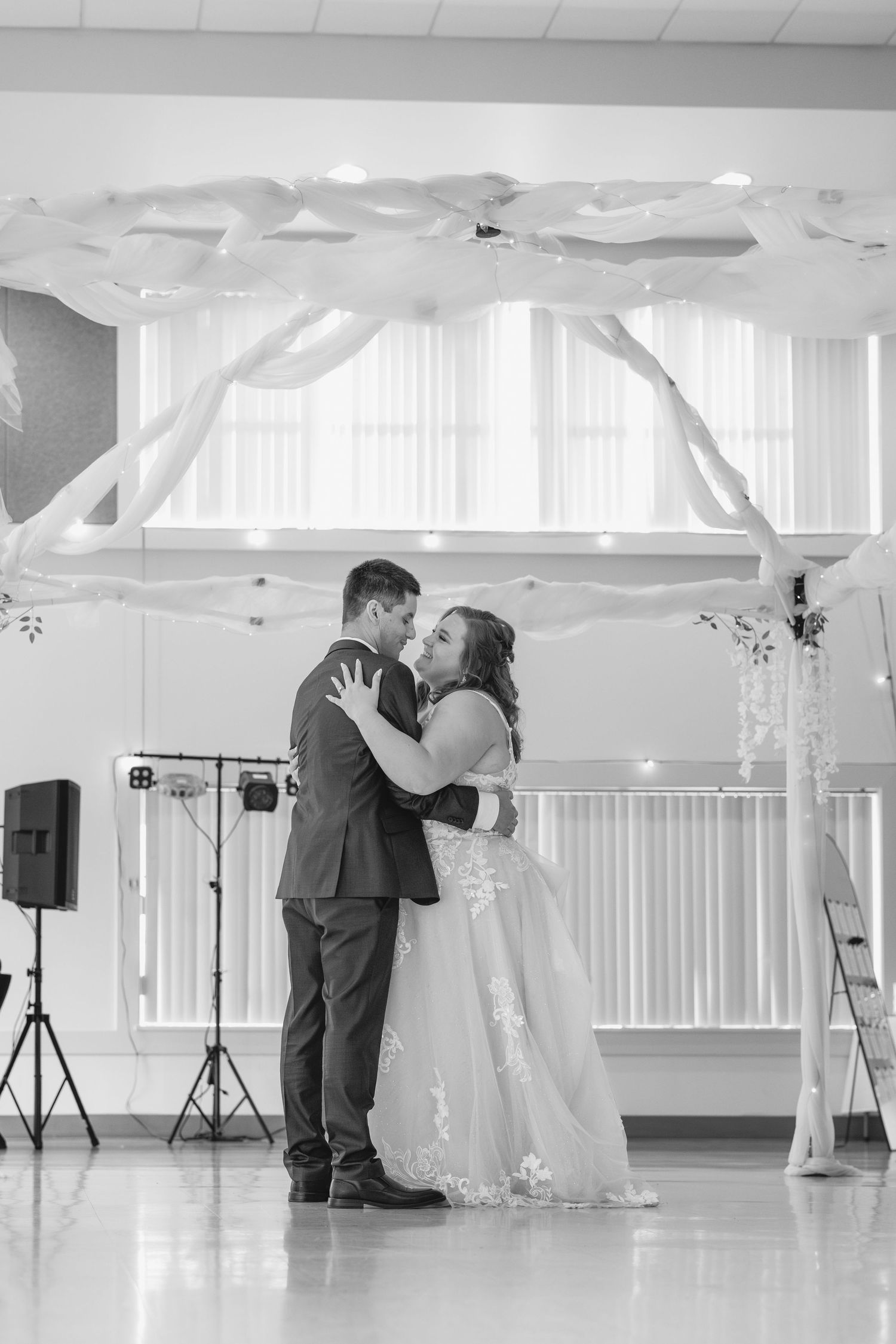 A couple shares their first dance under white fabric decorations in a reception hall.