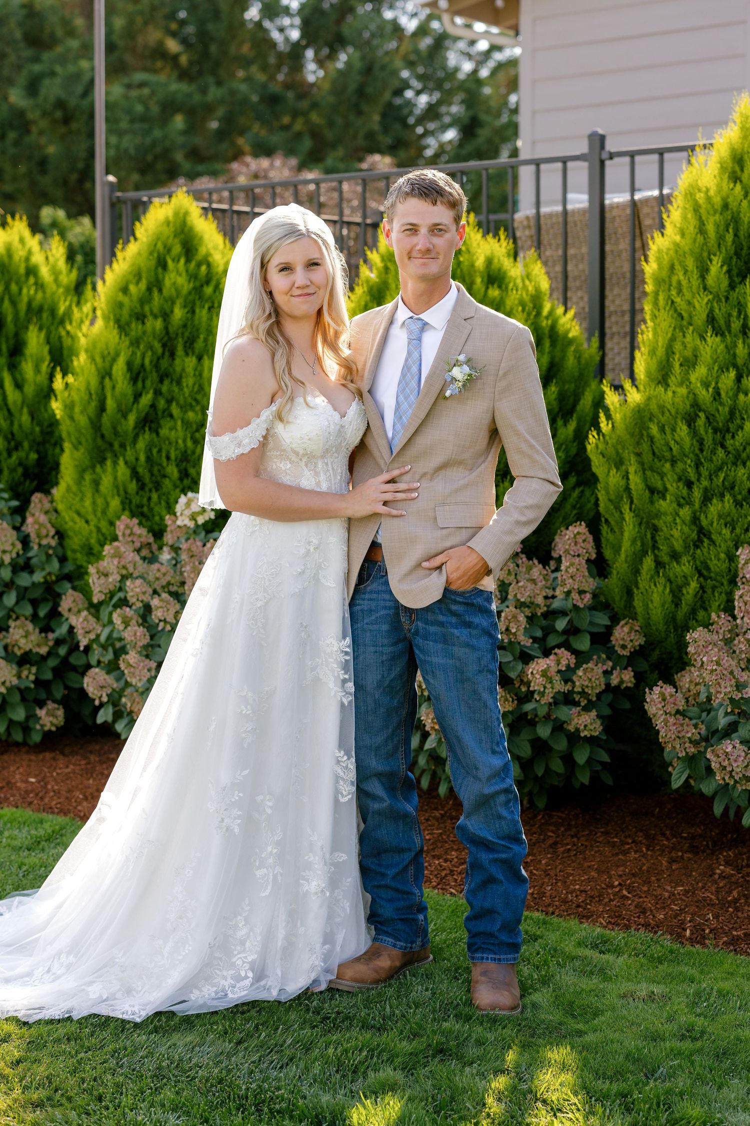 Wedding portraits taken in a garden setting with evergreen shrubs and landscaping.