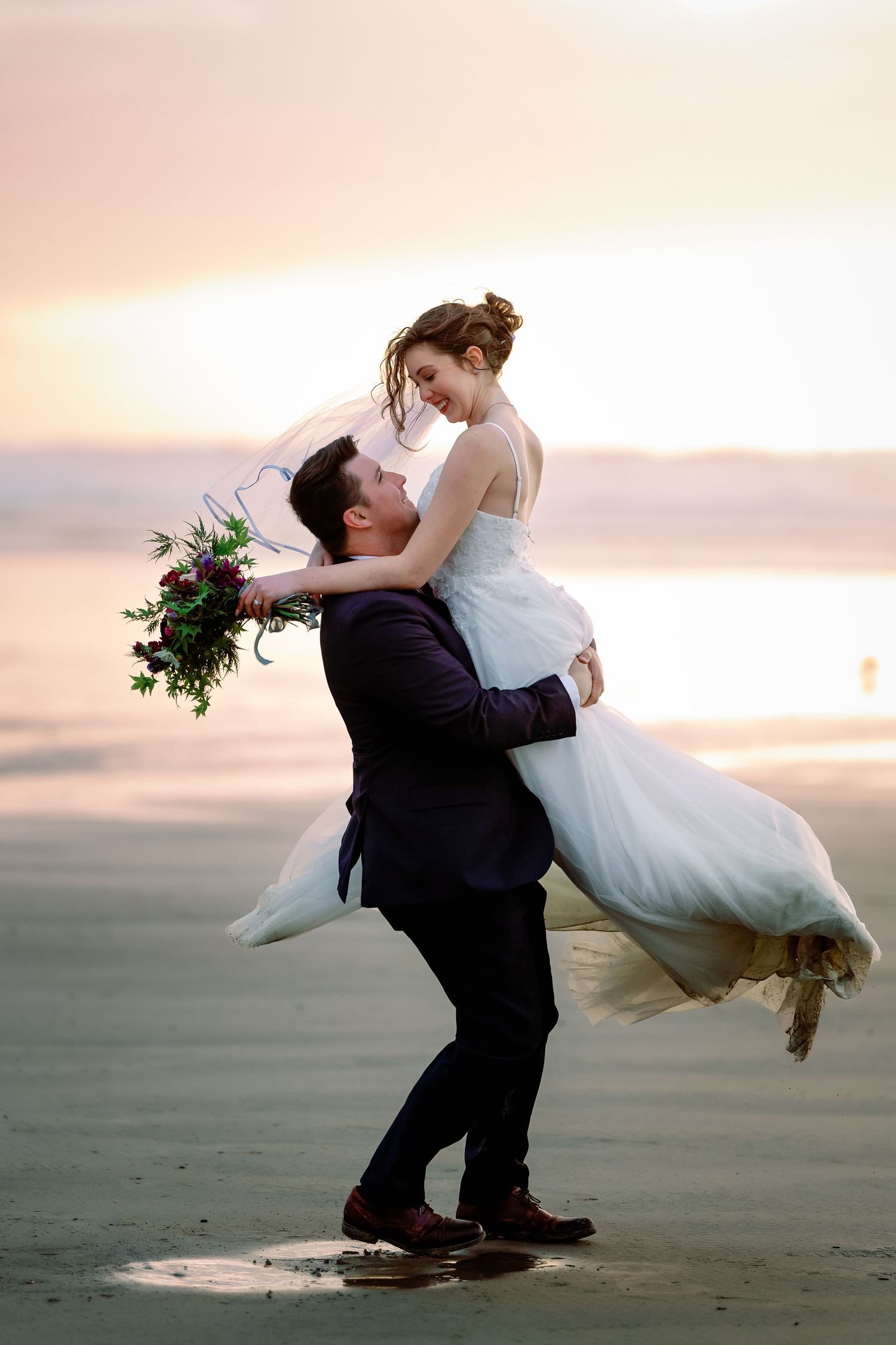 A groom sweeps his bride off her feet in a romantic sunset dance on the beach.