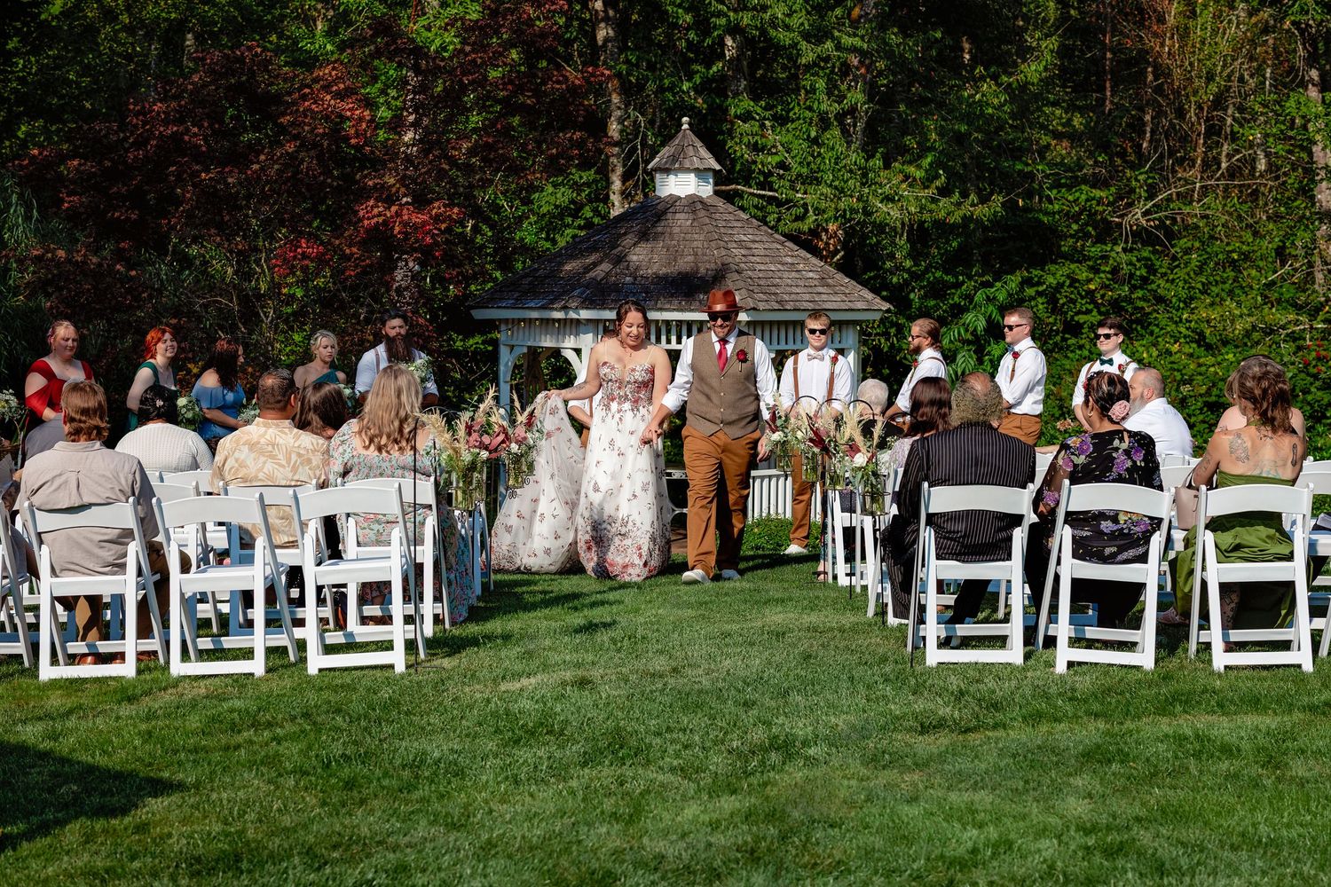 White chairs set up for outdoor garden wedding ceremony with guests seated.