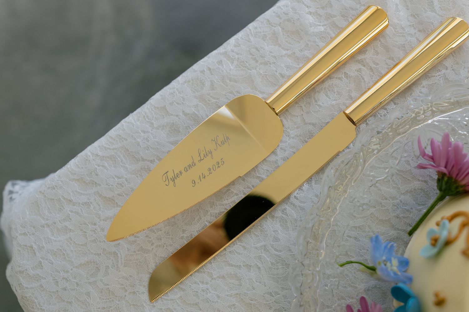 Gold wedding cake serving set displayed on white textured tablecloth with floral details.