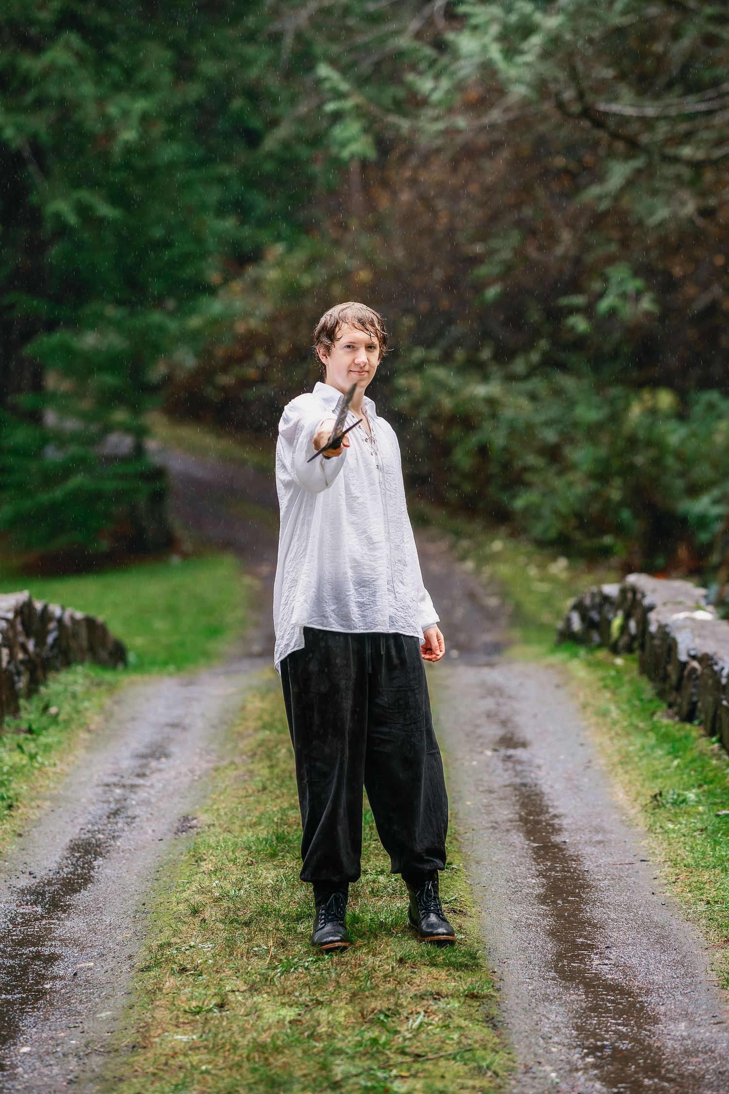 A person in white shirt and black pants stands on a rural dirt path surrounded by greenery.