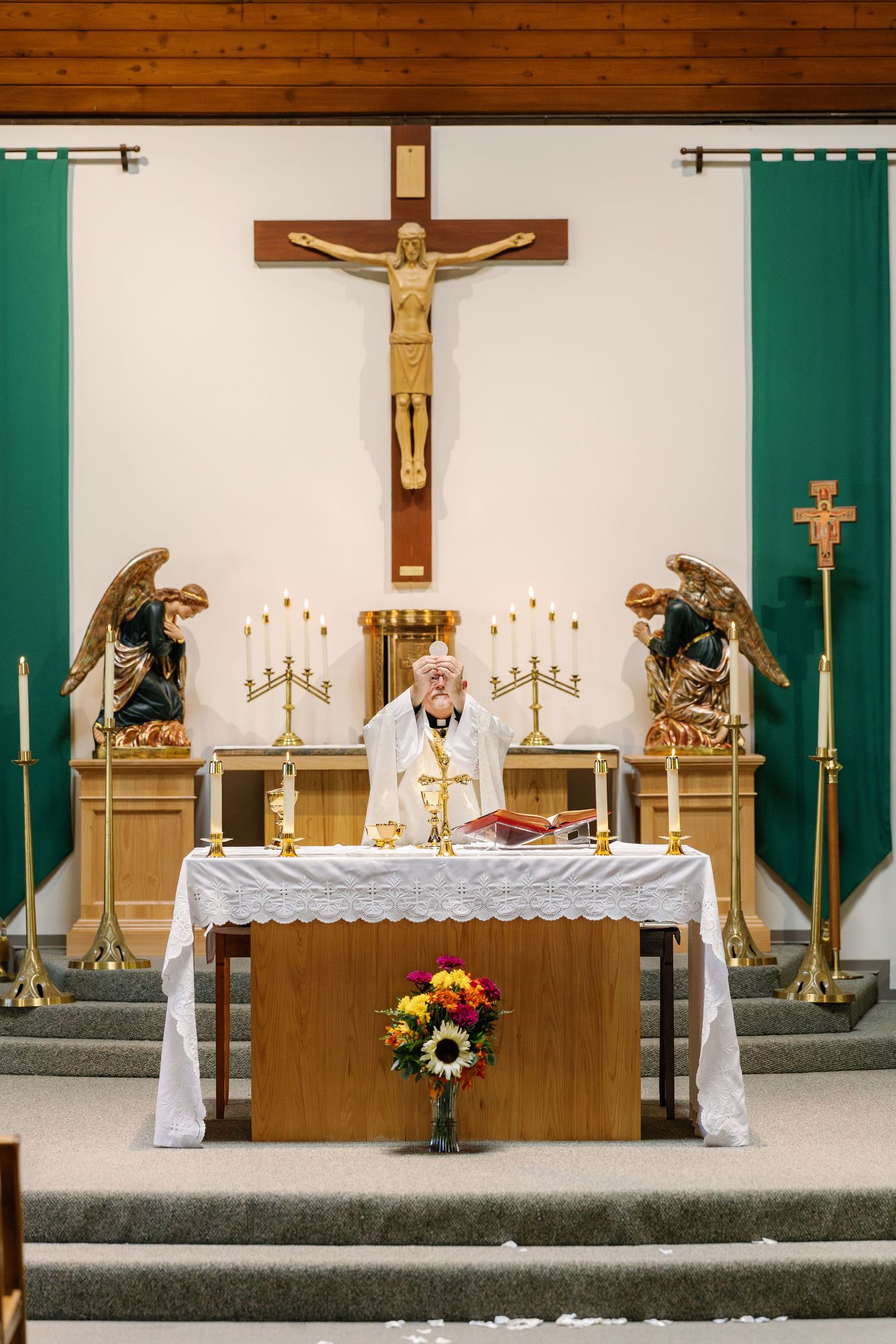 Church altar decorated for a wedding ceremony with crosses, candles, and floral arrangements in green and white.
