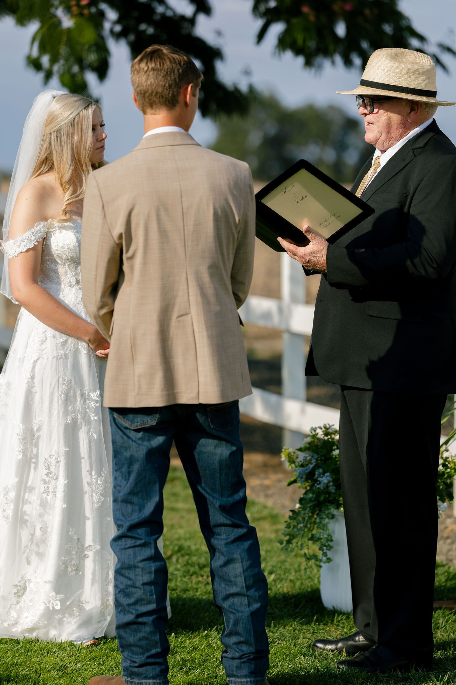Outdoor wedding ceremony with guests in casual attire and formal wear on a grassy lawn.