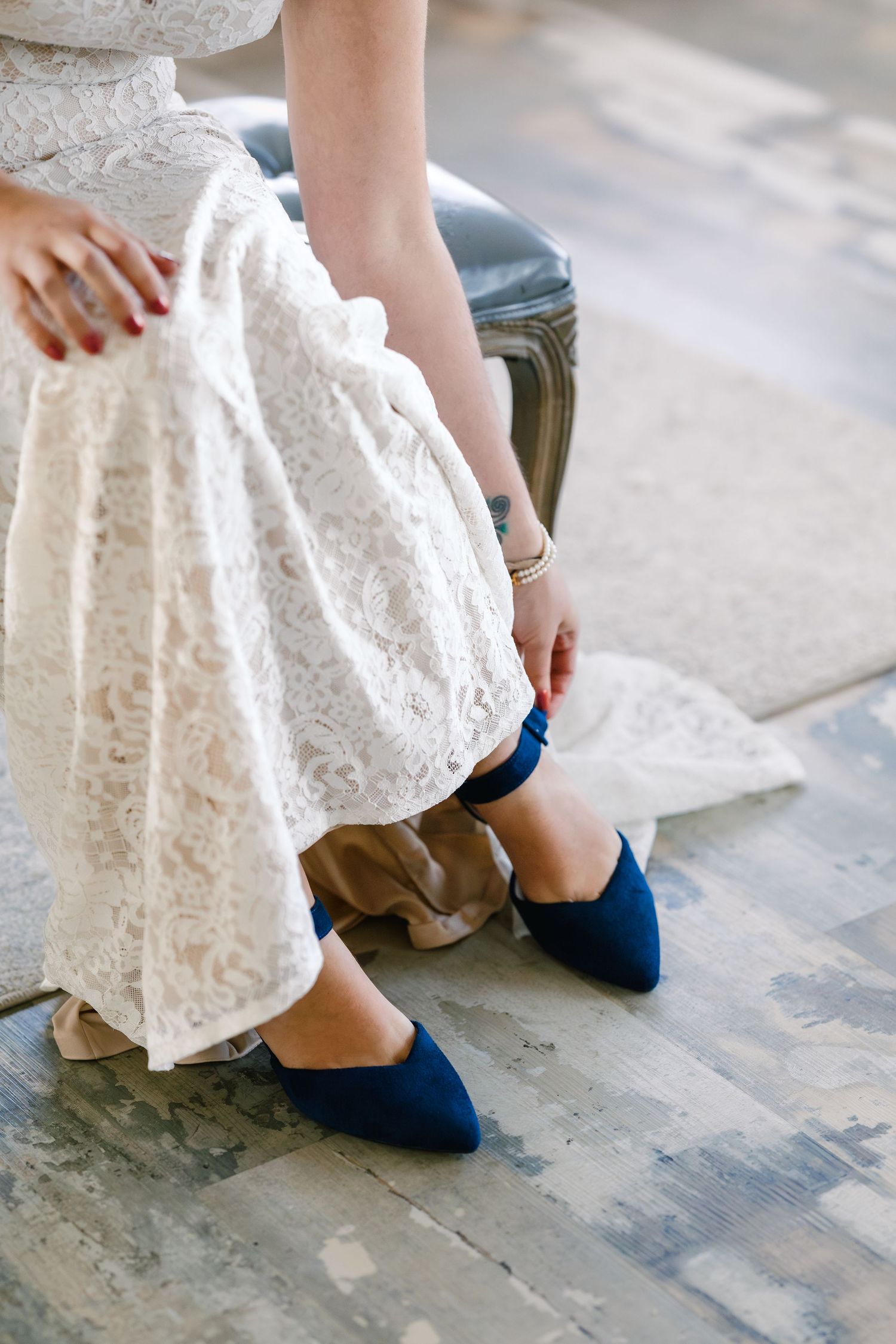 Close-up view of navy blue flats worn with a white lace dress on a concrete floor.