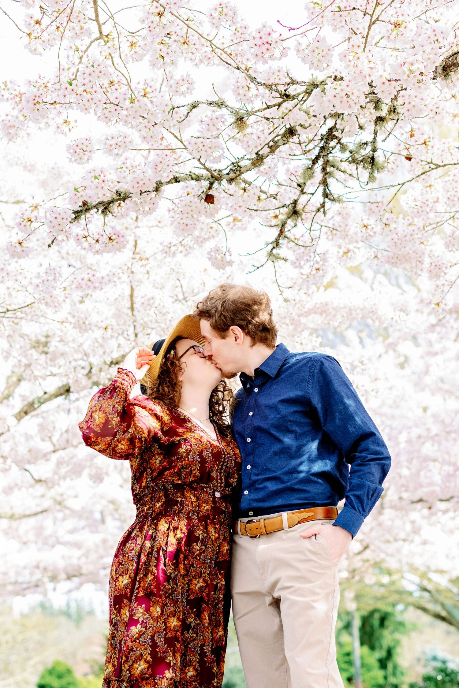 A couple embraces beneath delicate pink cherry blossoms on a bright spring day.