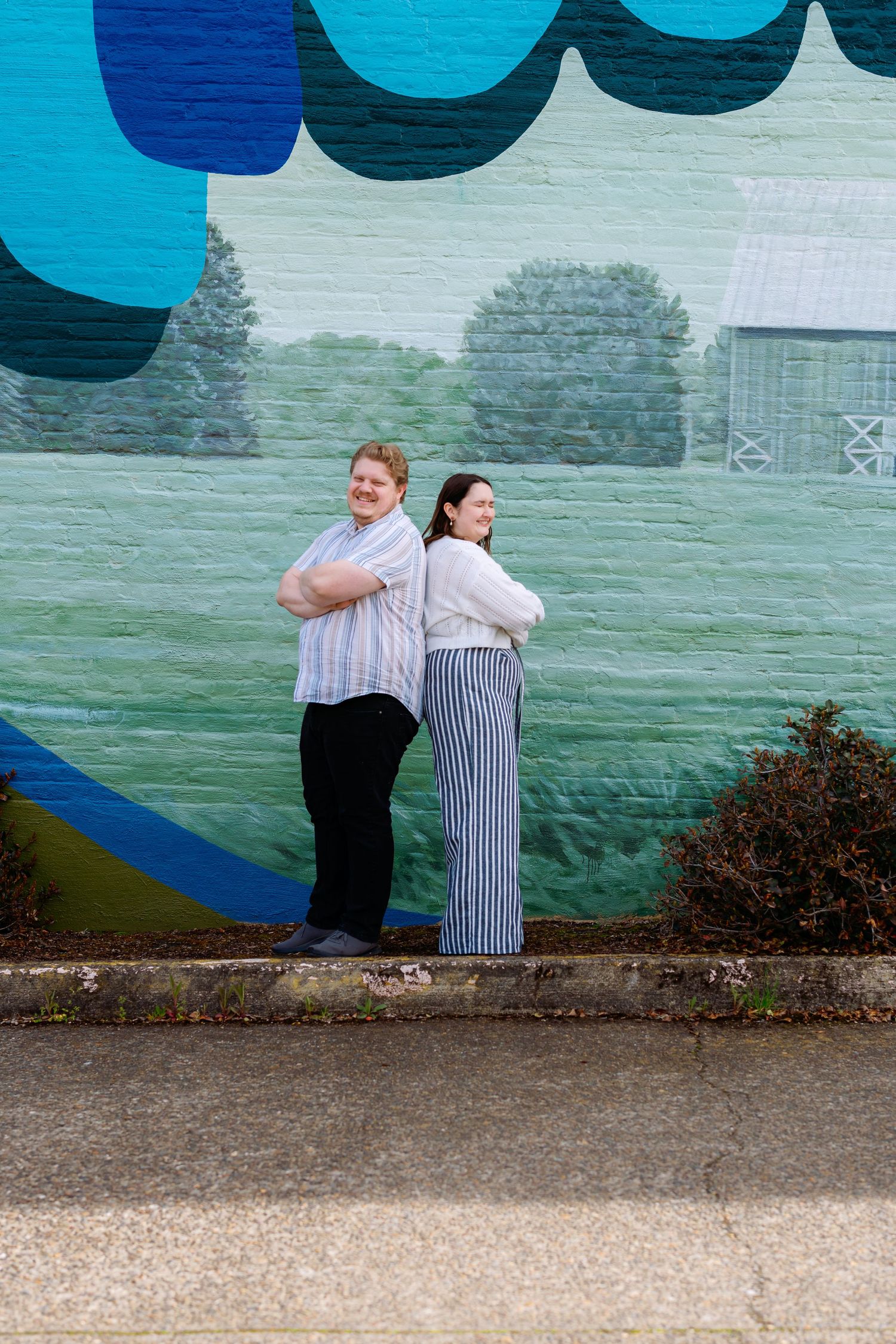 Couple in stripes posing back-to-back against vibrant blue mural wall.