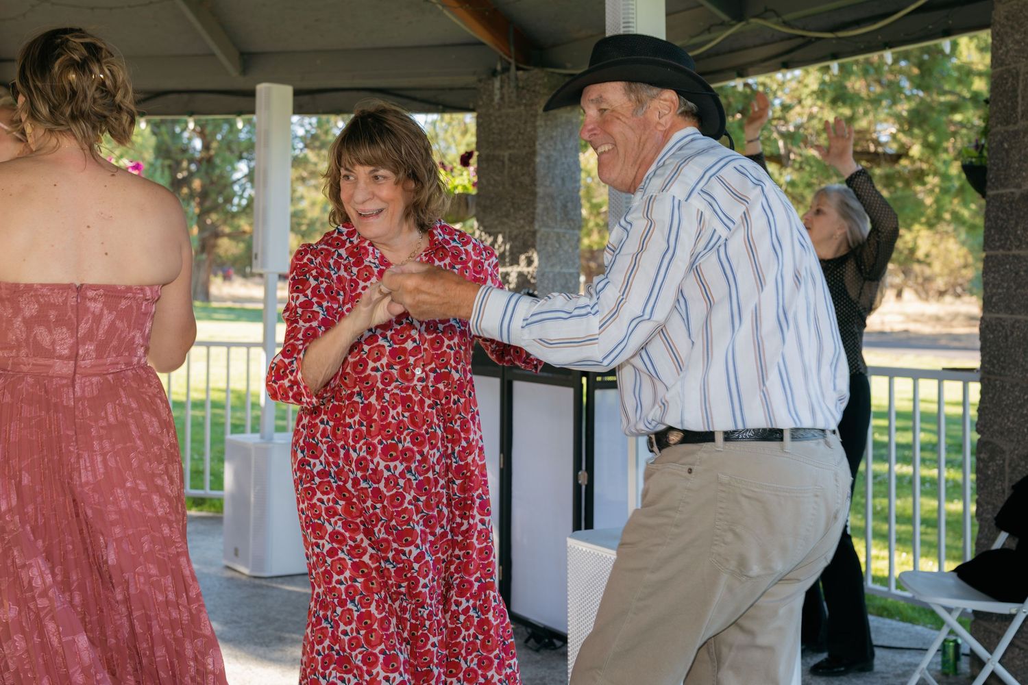 Older couple dancing joyfully together under a pavilion at an outdoor wedding reception celebration.