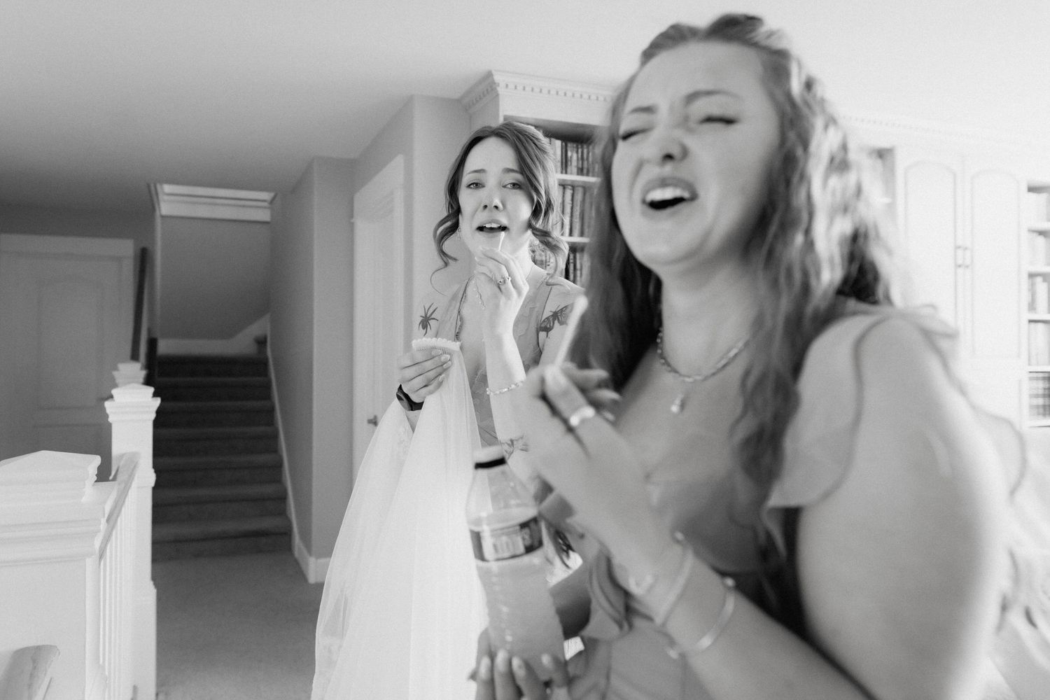 Bride and bridesmaid share an emotional laughing moment during wedding preparations in black and white.