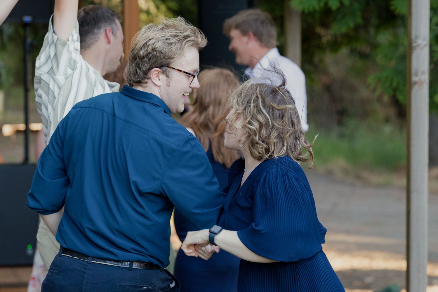 Two guests in blue outfits share a joyful dance moment at an outdoor wedding reception.