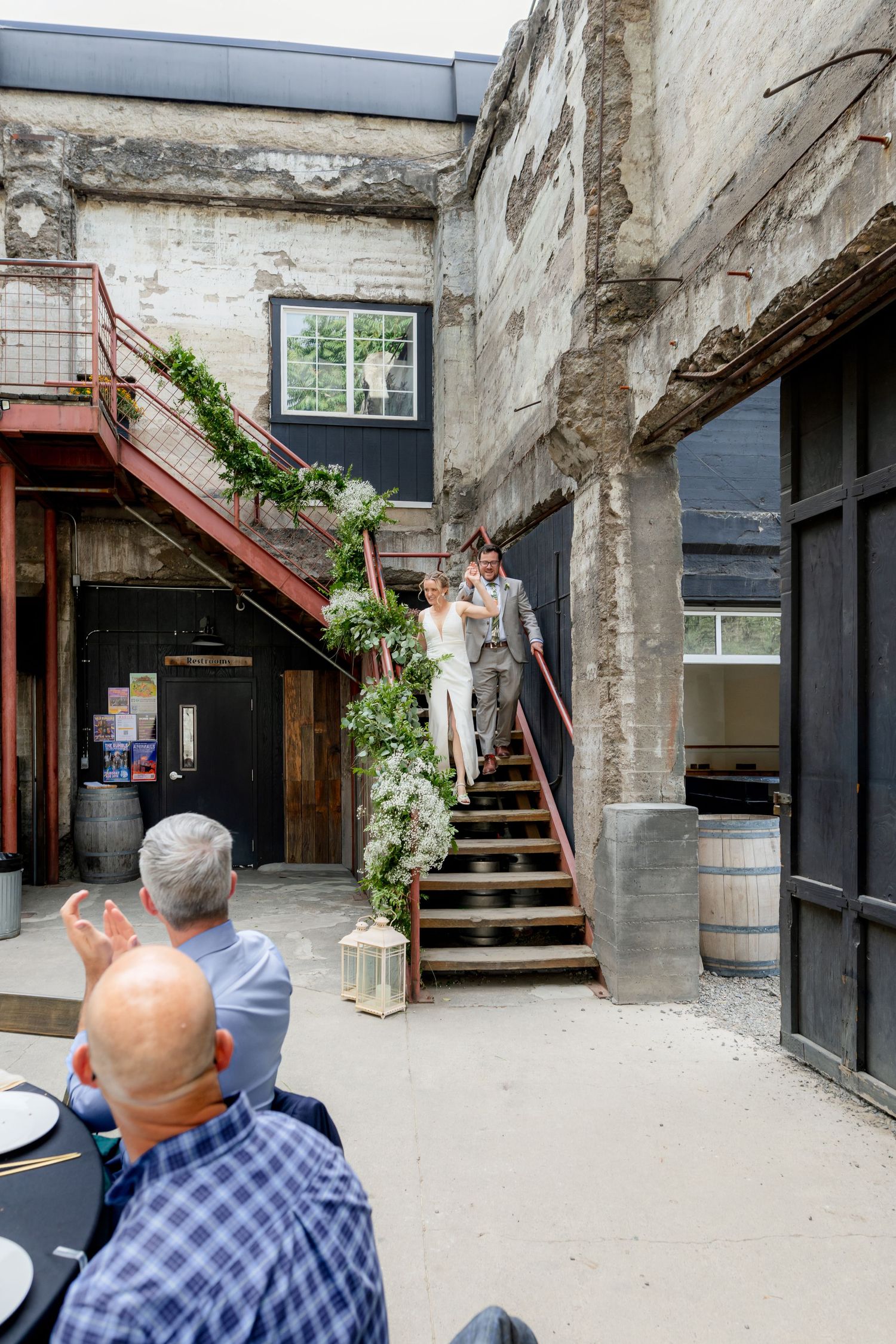 Newlyweds descend decorated industrial staircase as wedding guests applaud their entrance.