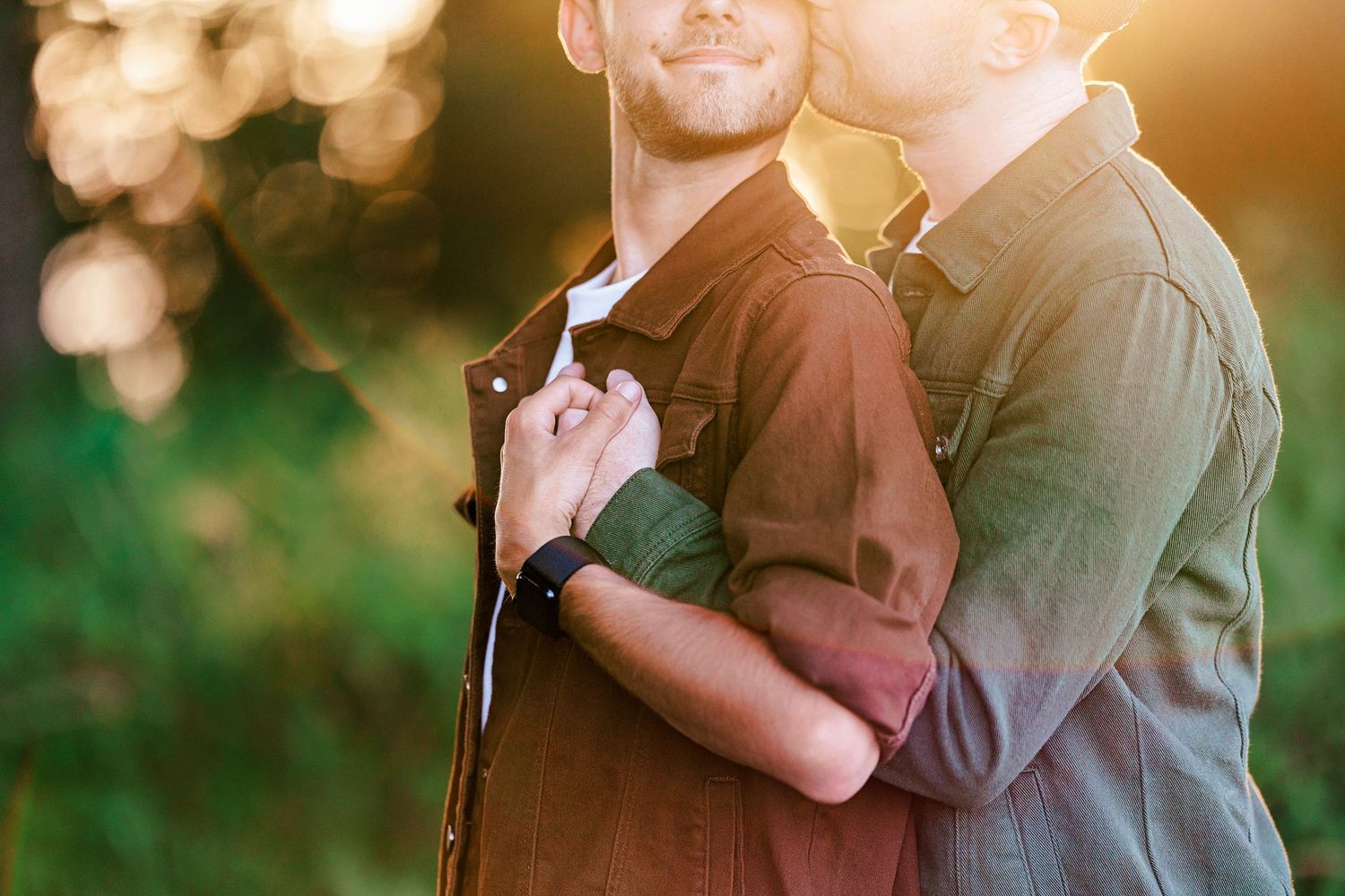 A romantic couple embraces during a golden hour photoshoot in a sunlit outdoor setting.