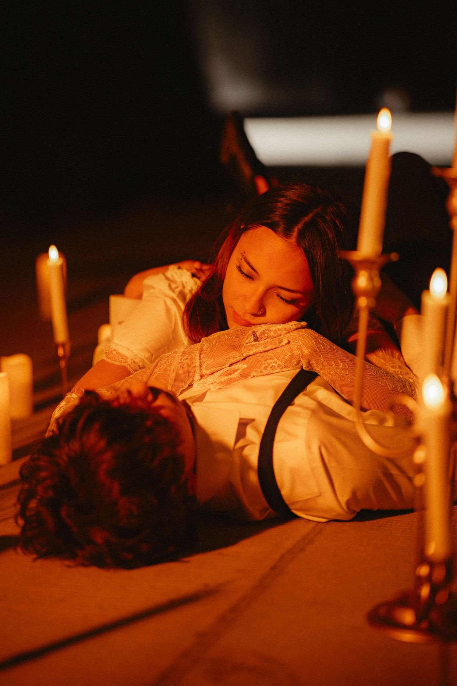 Candlelit scene with figures in vintage white dresses resting on a dark surface.