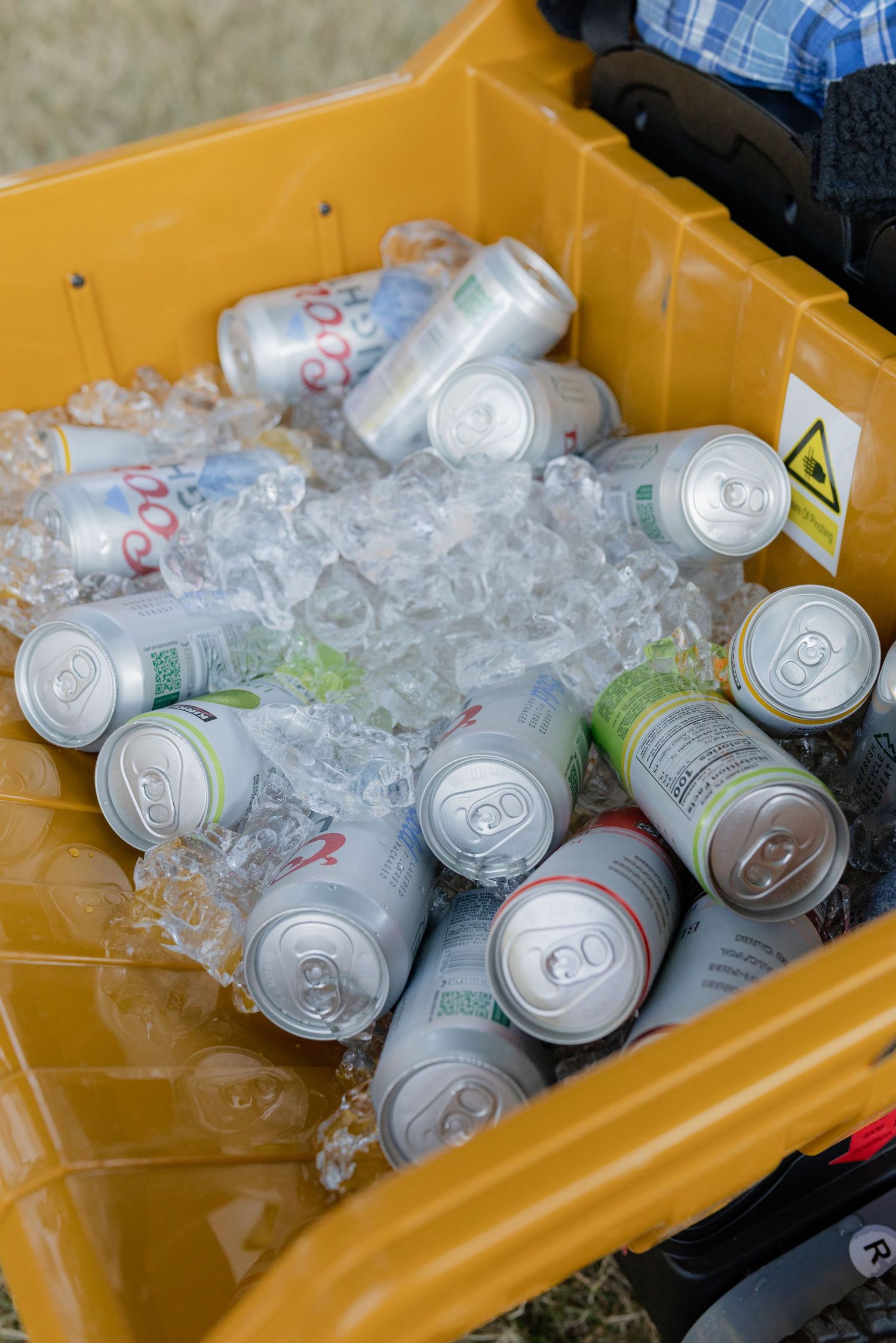 Yellow wagon cooler filled with assorted canned beverages and ice at an outdoor wedding reception.