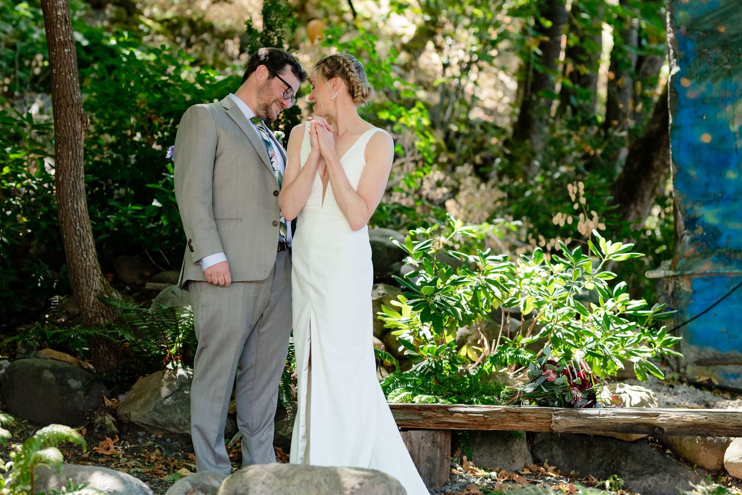 Bride and groom share an intimate moment in a lush garden setting, bride in white gown, groom in gray suit.