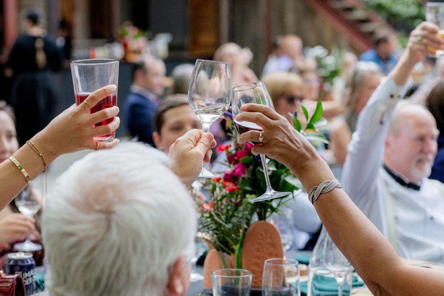 Guests raising glasses in a celebratory toast at an outdoor wedding reception with floral centerpieces.