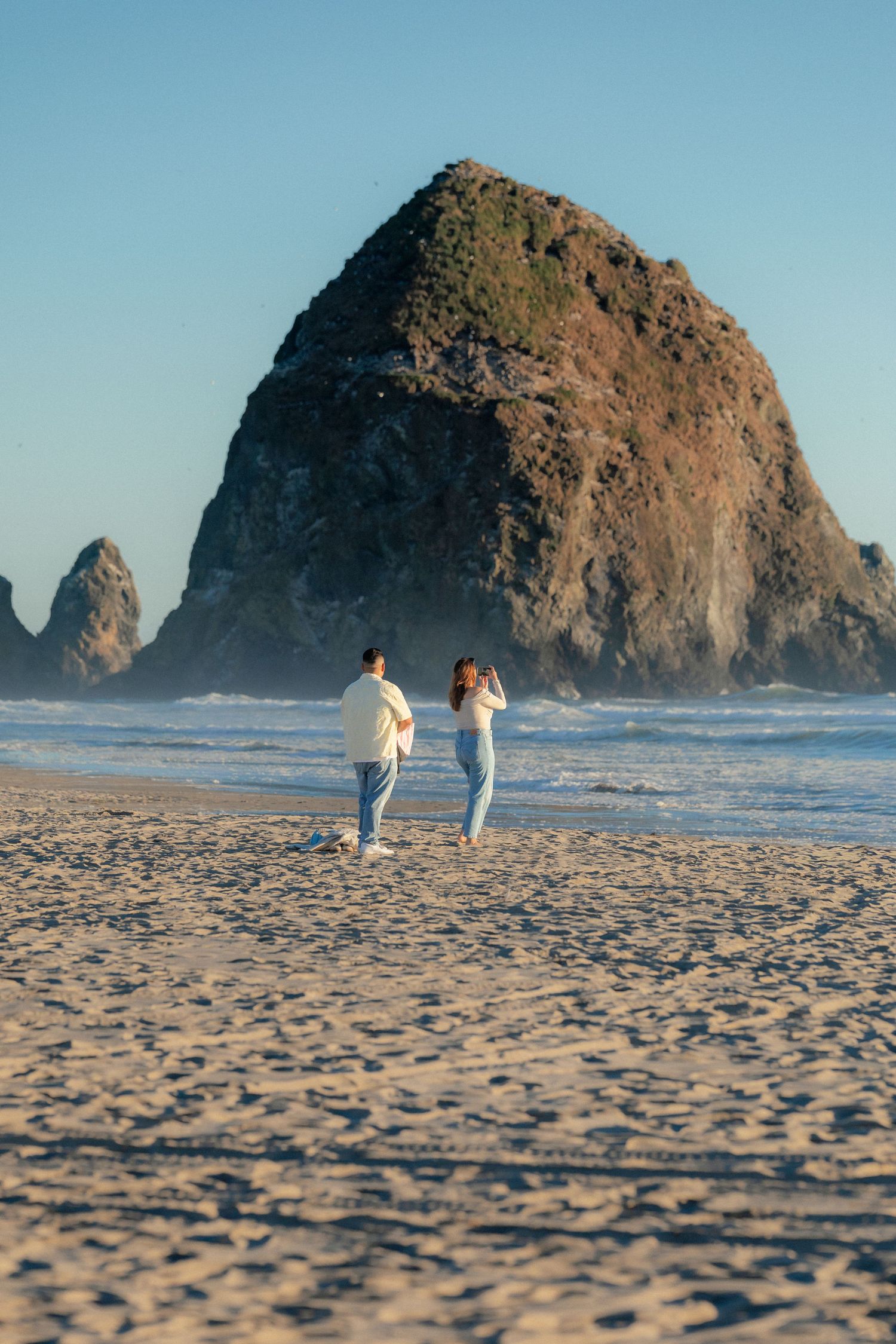 Couple walking on sandy beach toward iconic Haystack Rock at Cannon Beach, Oregon on a clear sunny day.