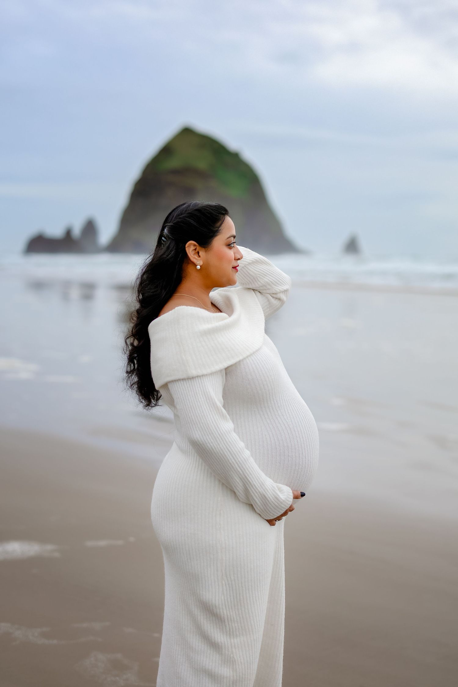 A person in a cozy white sweater stands contemplatively on a misty beach with rocky sea stacks in the background.
