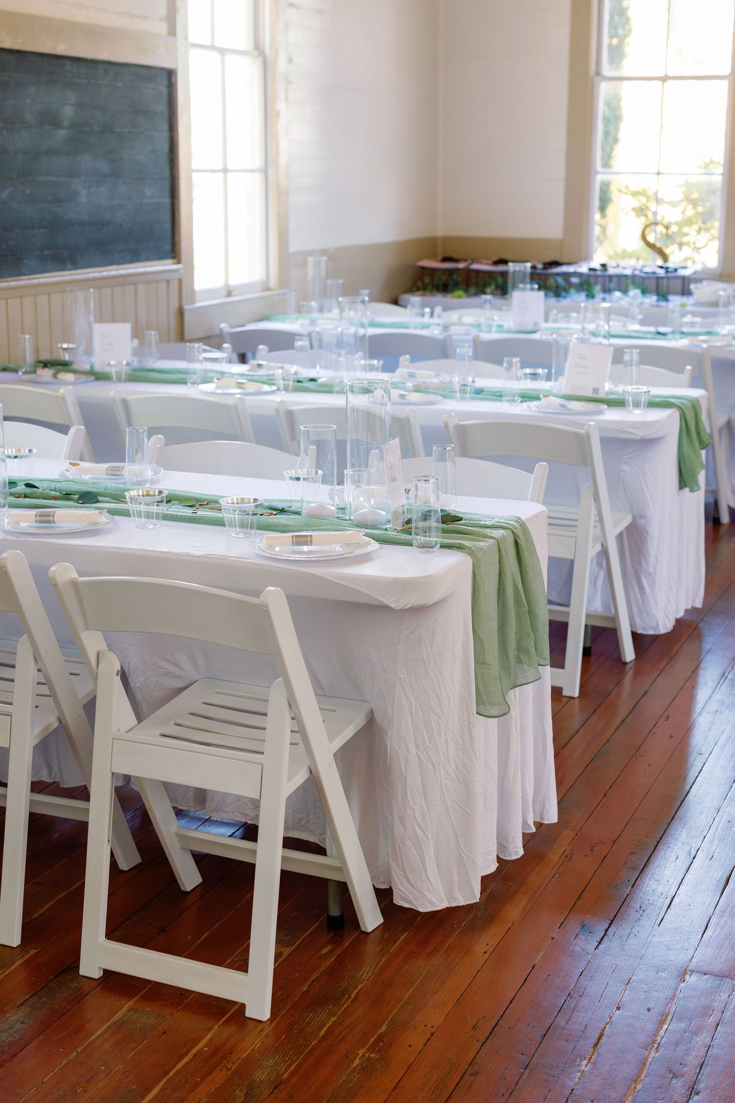 Reception tables set with white linens and green accents in a bright room with hardwood floors.