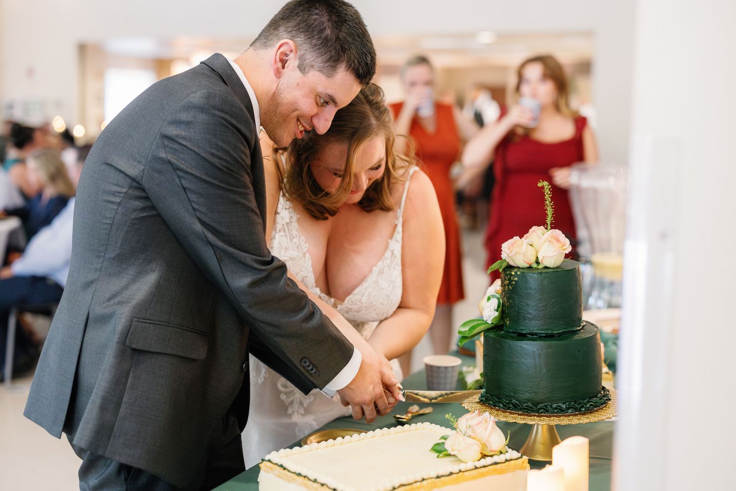A couple cuts into an elegant dark green and gold wedding cake together.