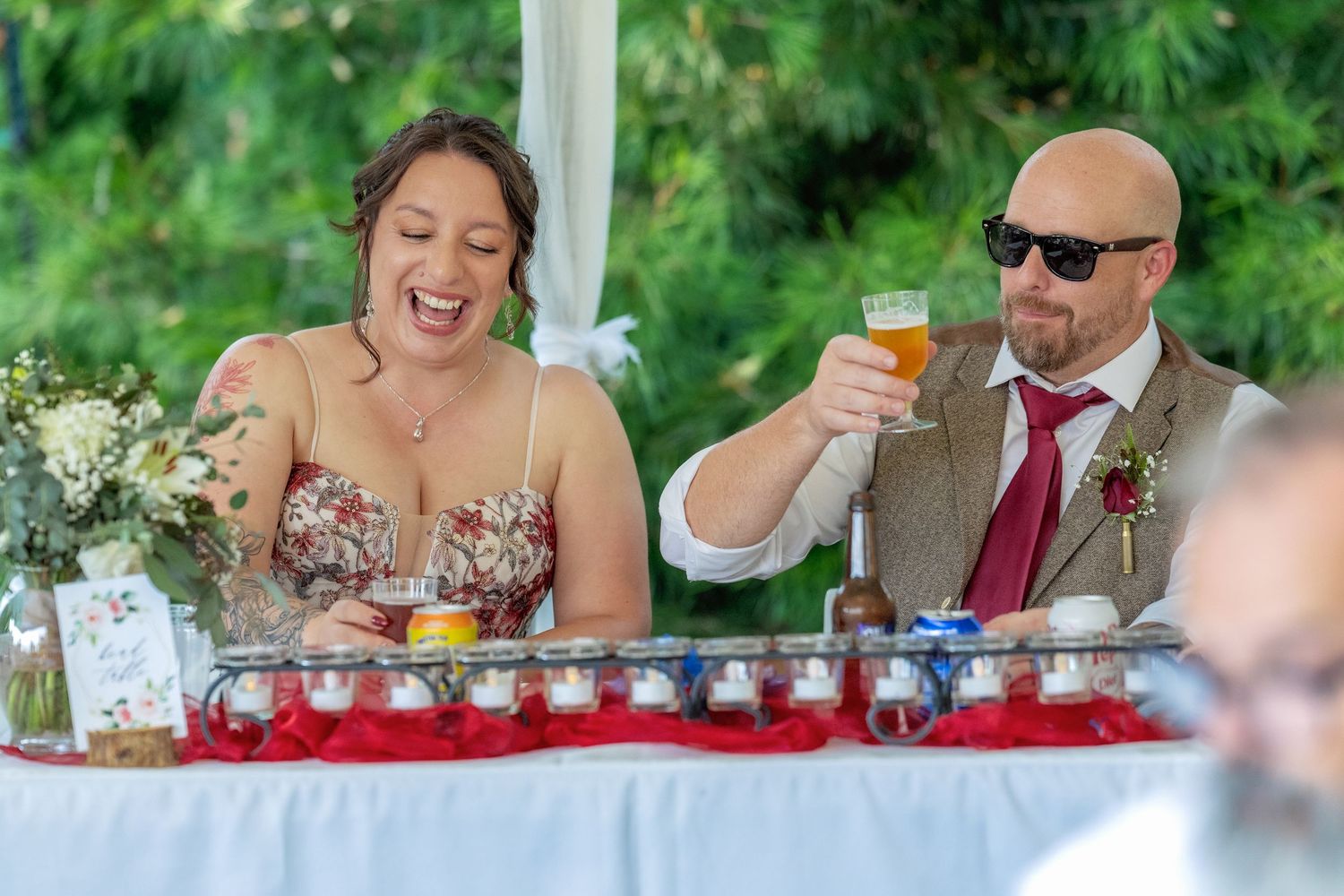 Wedding guests enjoy drinks and laughter during an outdoor garden reception celebration.