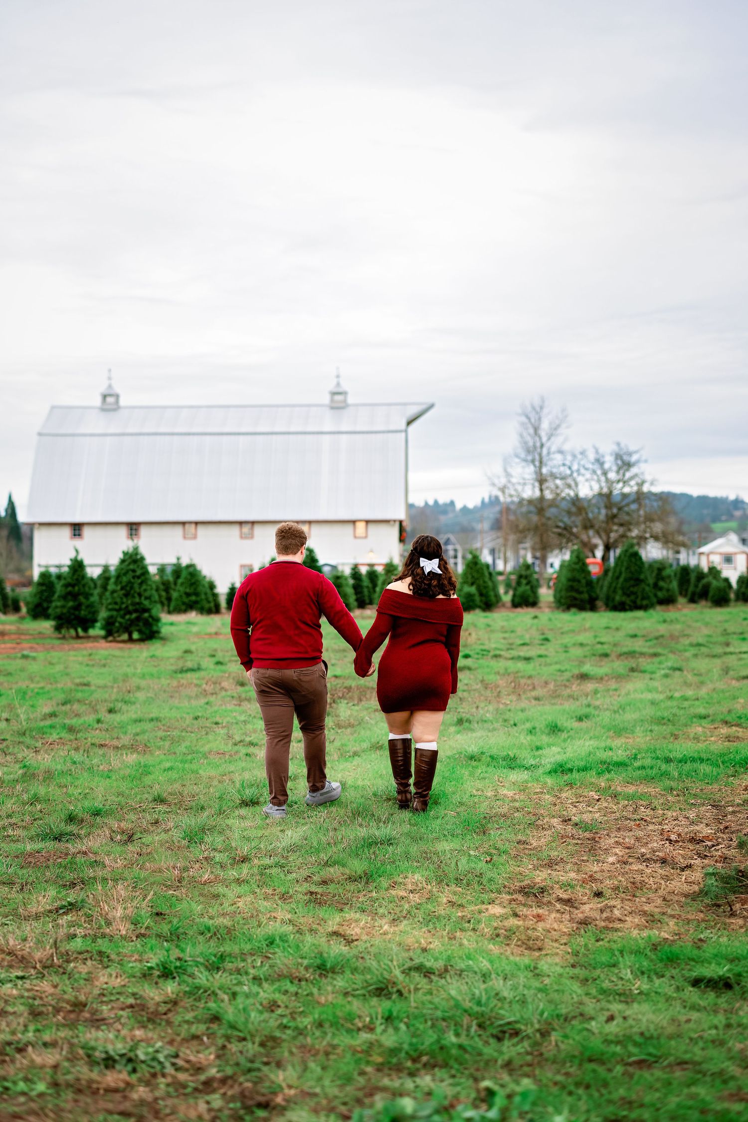 A couple in matching red sweaters walks together through a green field on an overcast day.