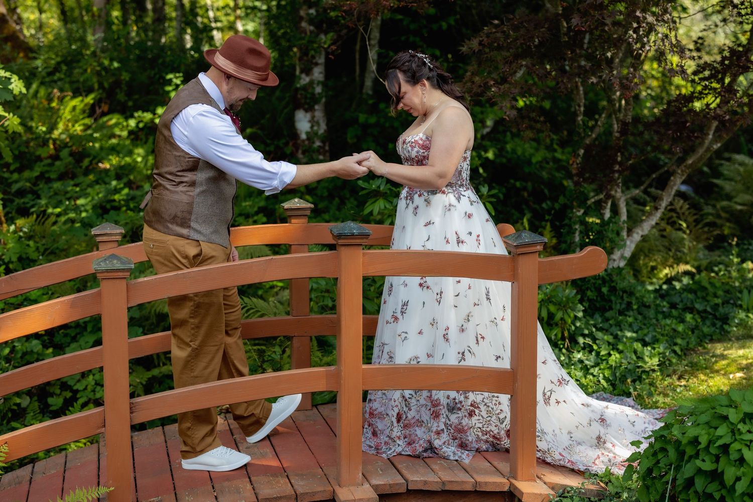 Wooden bridge in a garden setting decorated with floral arrangements and white fabric draping for a wedding ceremony.