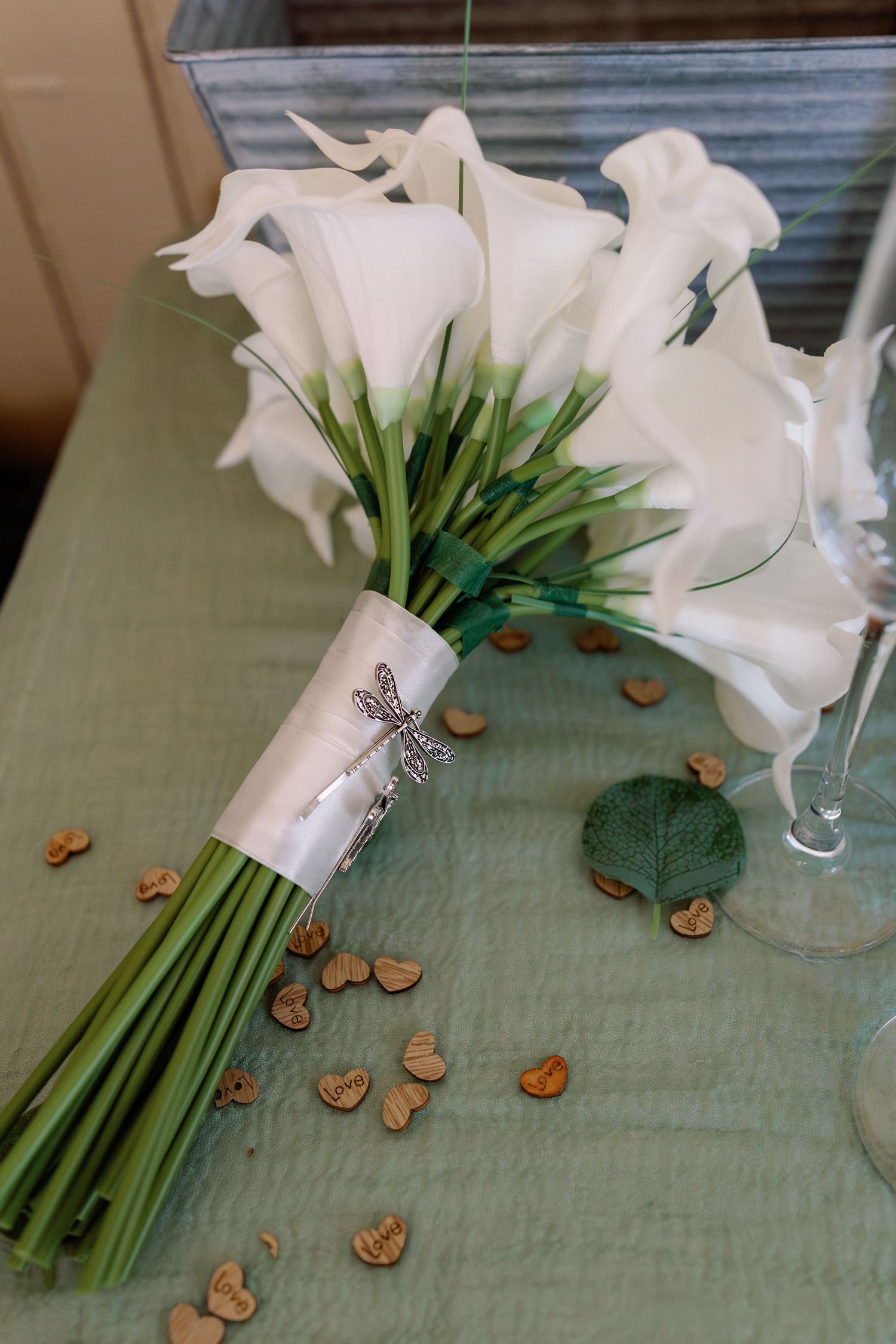 Elegant white calla lily bridal bouquet with ribbon wrap and scattered wooden heart decorations.