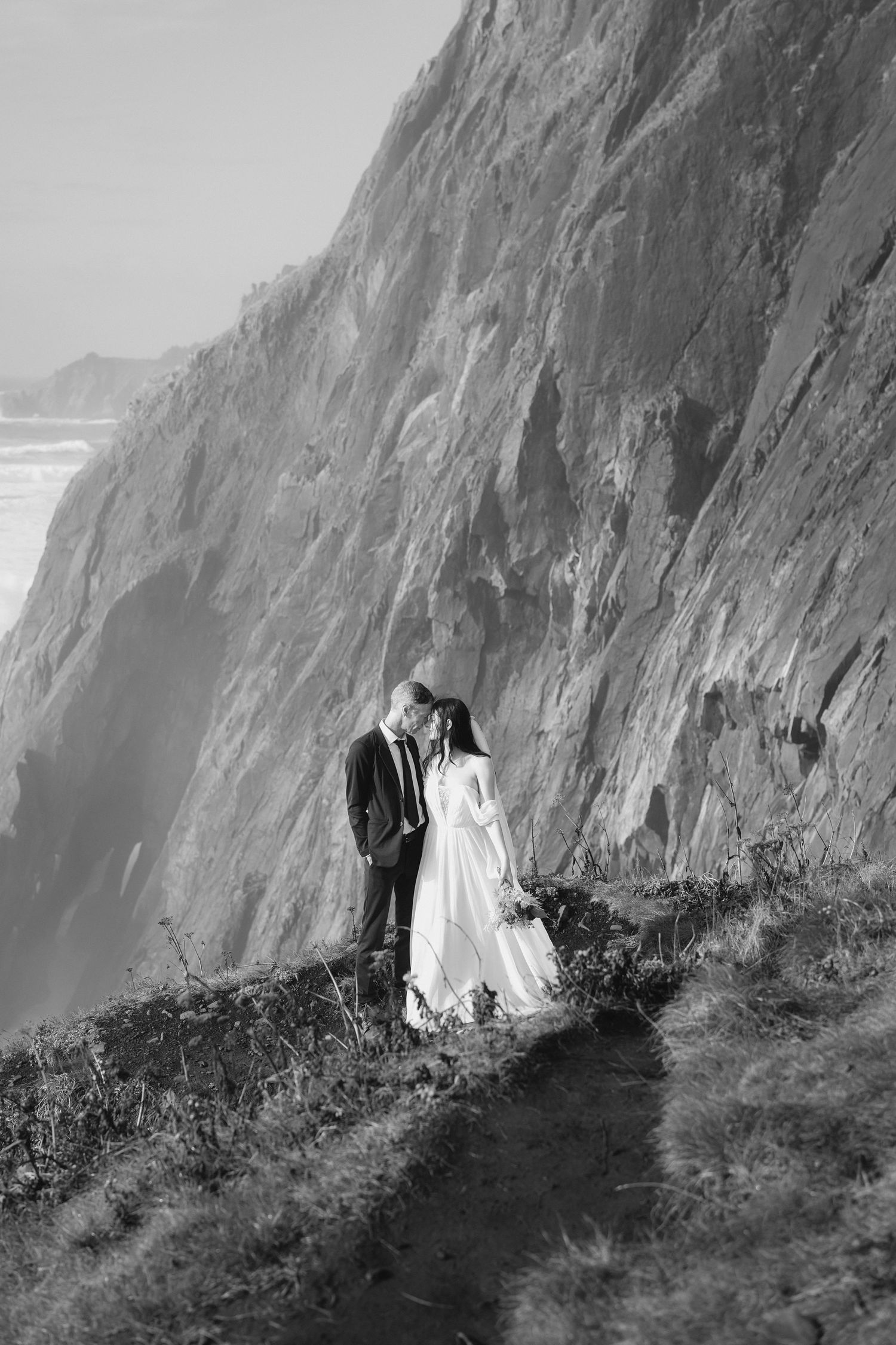 A black and white wedding photo sequence shows a couple posing along a dramatic coastal cliff edge.
