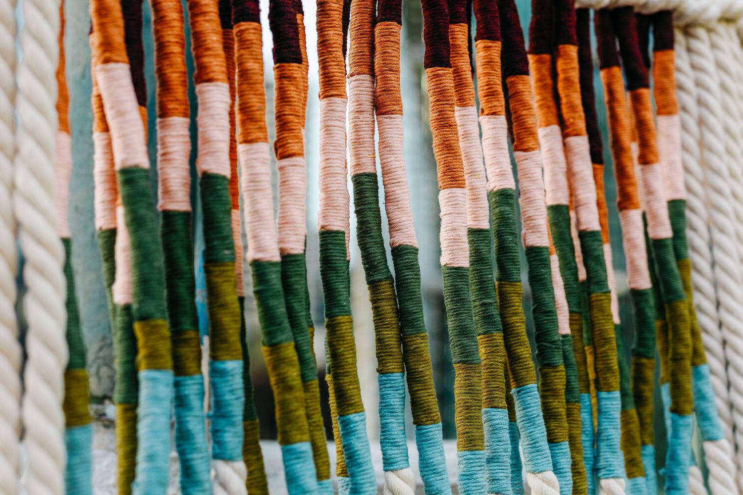 Colorful woven threads in orange, green and blue hanging in a decorative pattern.