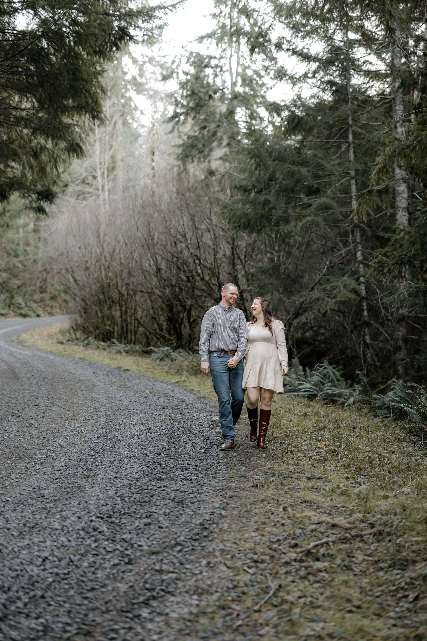 A couple walking together on a winding gravel path through an evergreen forest.