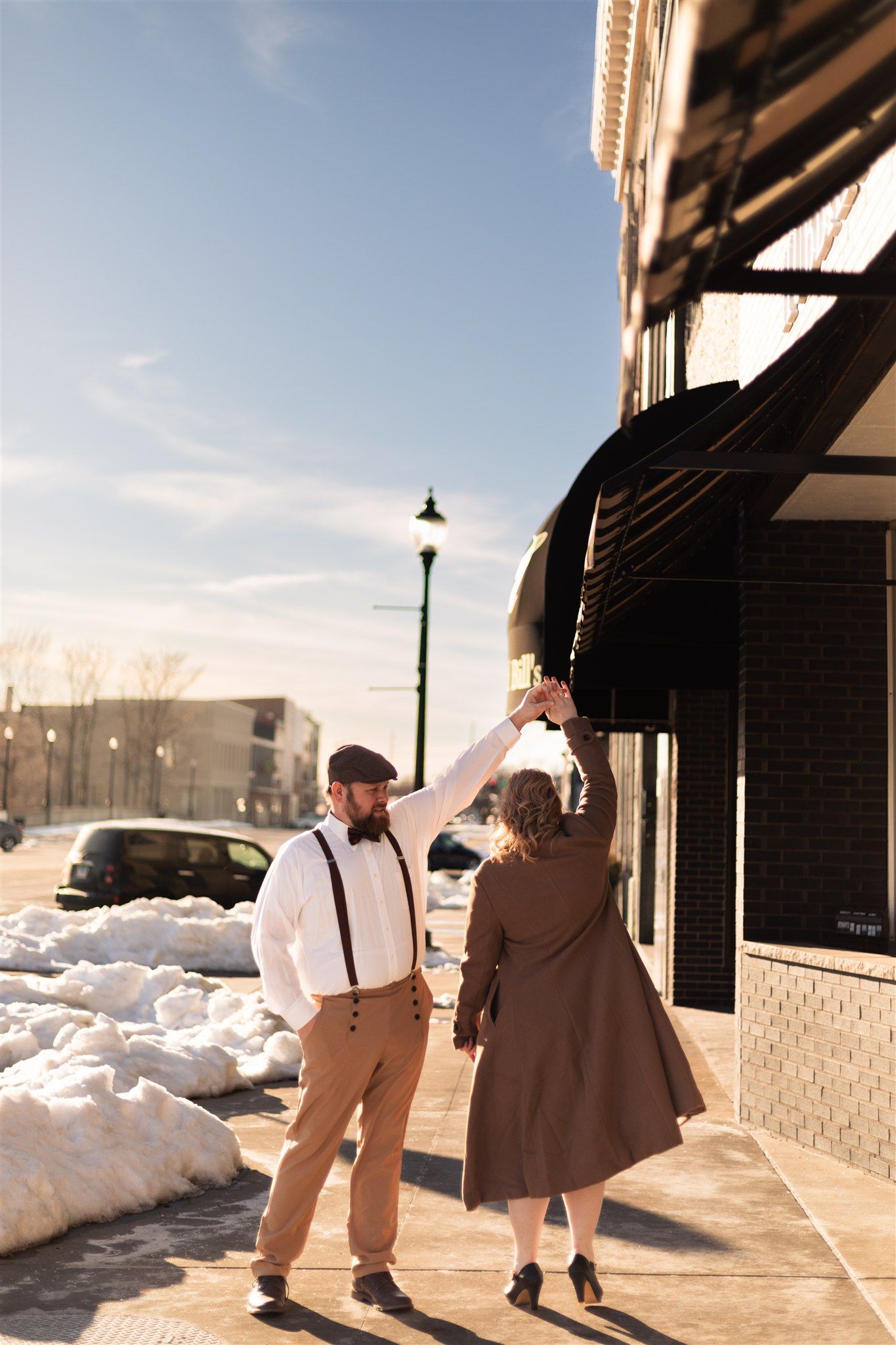 Couple dancing on sidewalk in vintage clothing with snow banks visible.