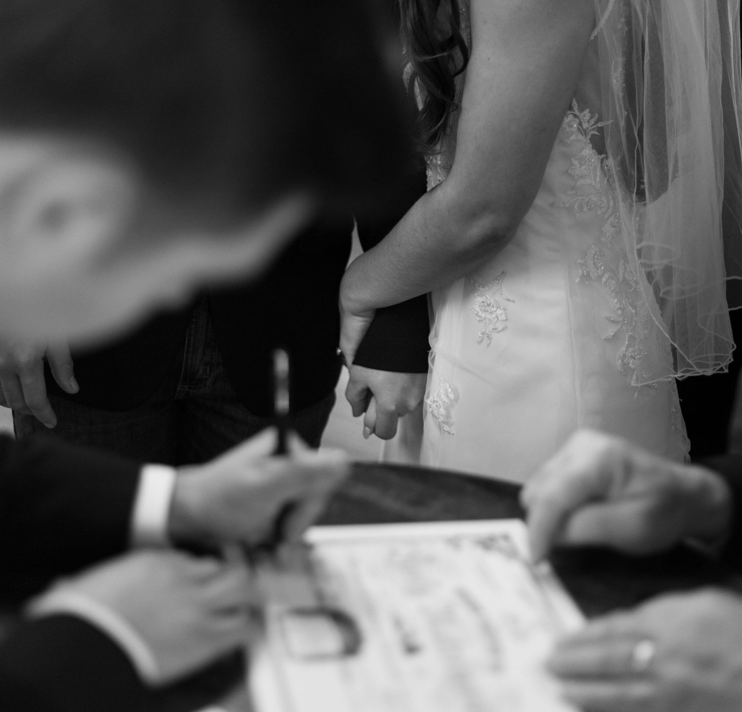 Black and white image showing hands signing a document with a pen during a formal ceremony.