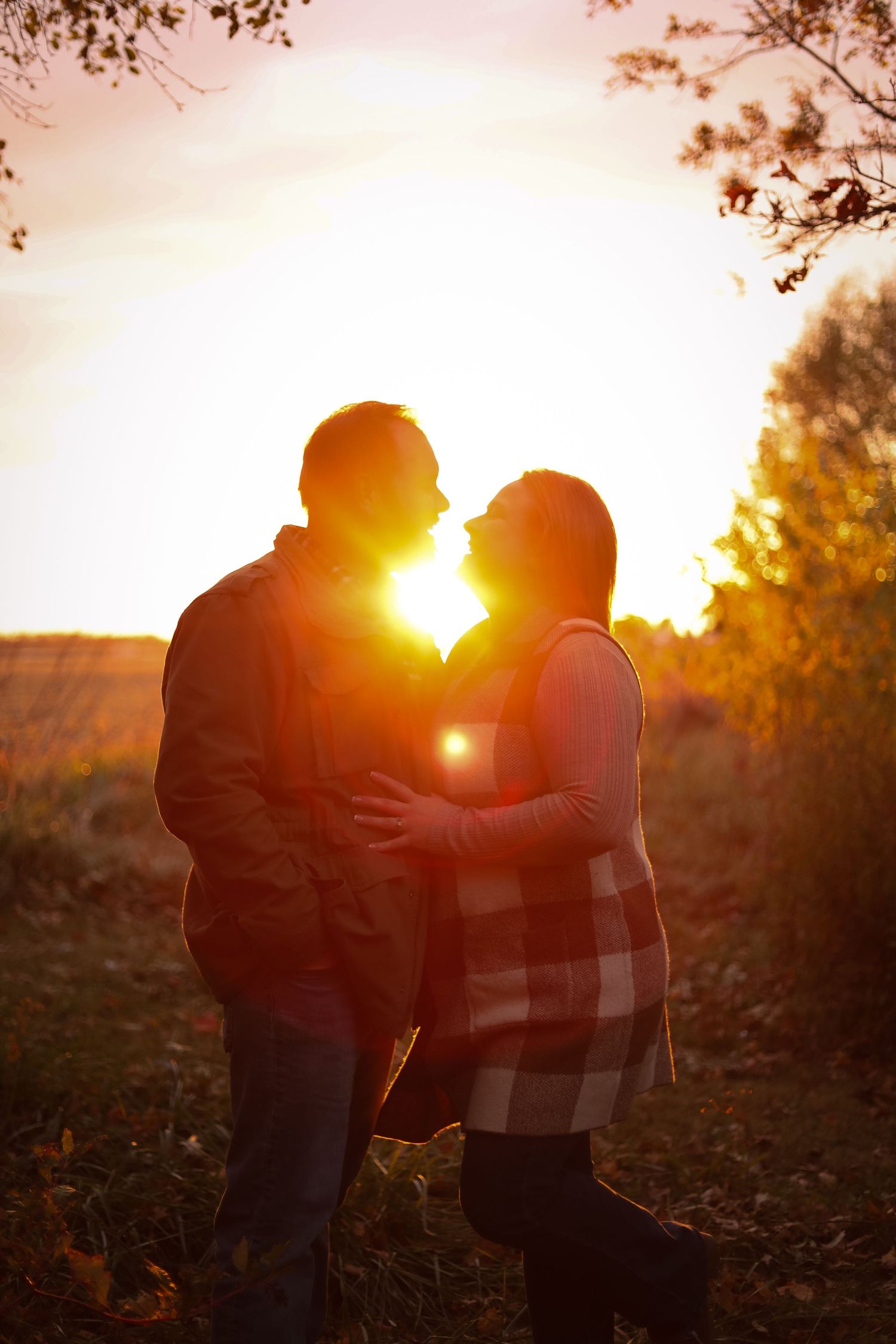 Silhouetted couple embracing in a golden sunset with autumn trees in the background.