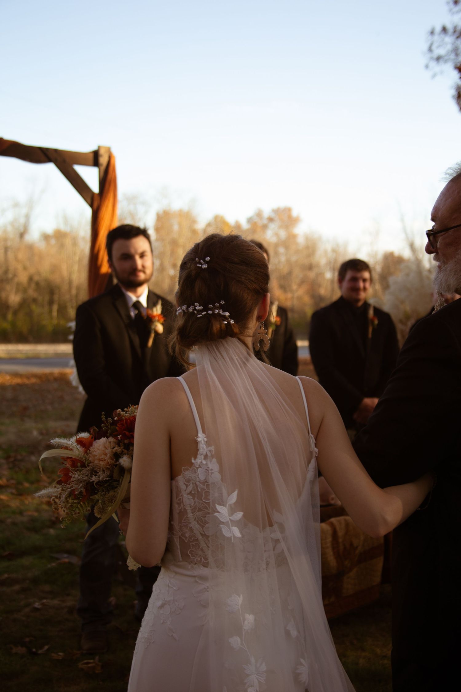 Wedding ceremony takes place outdoors at sunset with guests gathered around the couple in a natural setting.