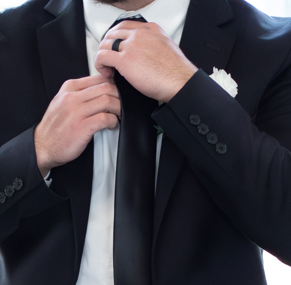Professional in black suit adjusts white necktie in sequence of close-up shots.