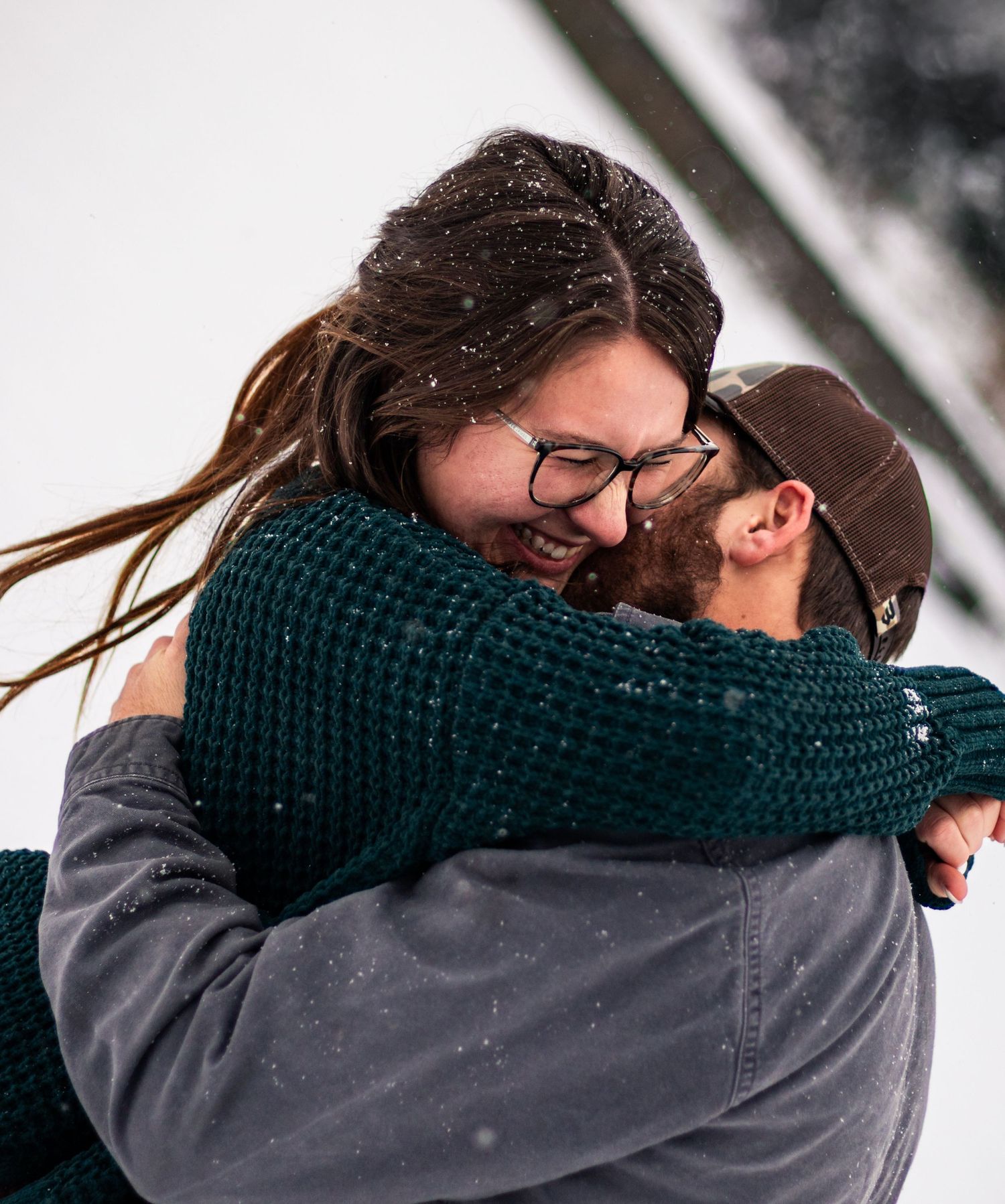 Close-up of couple hugging in winter with snow falling around them.